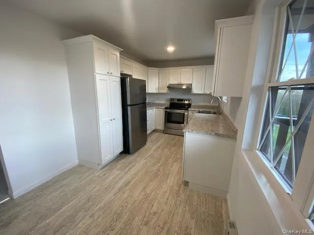 Kitchen featuring electric range, freestanding refrigerator, under cabinet range hood, light wood-style floors, and light stone counters Kitchen featuring electric range, freestanding refrigerator, under cabinet range hood, light wood-style floors, and light stone counters