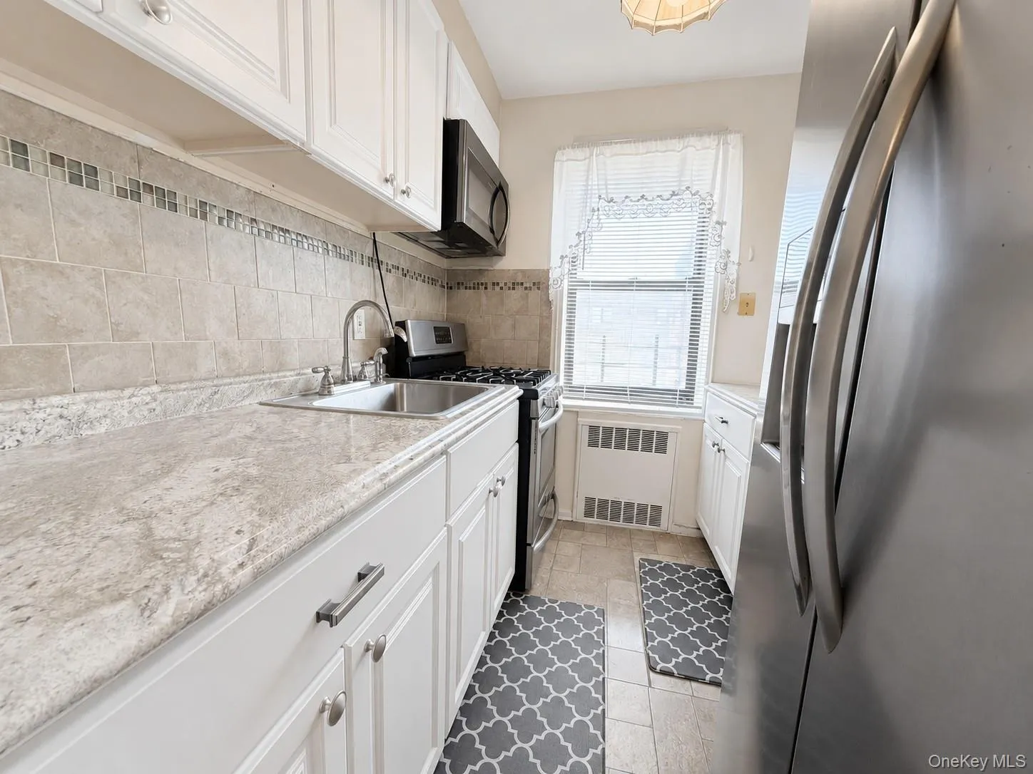 Kitchen featuring white cabinetry, light-toned countertops, tile backsplash with decorative accents, stainless steel sink, and built-in microwave Kitchen featuring white cabinetry, light-toned countertops, tile backsplash with decorative accents, stainless steel sink, and built-in microwave