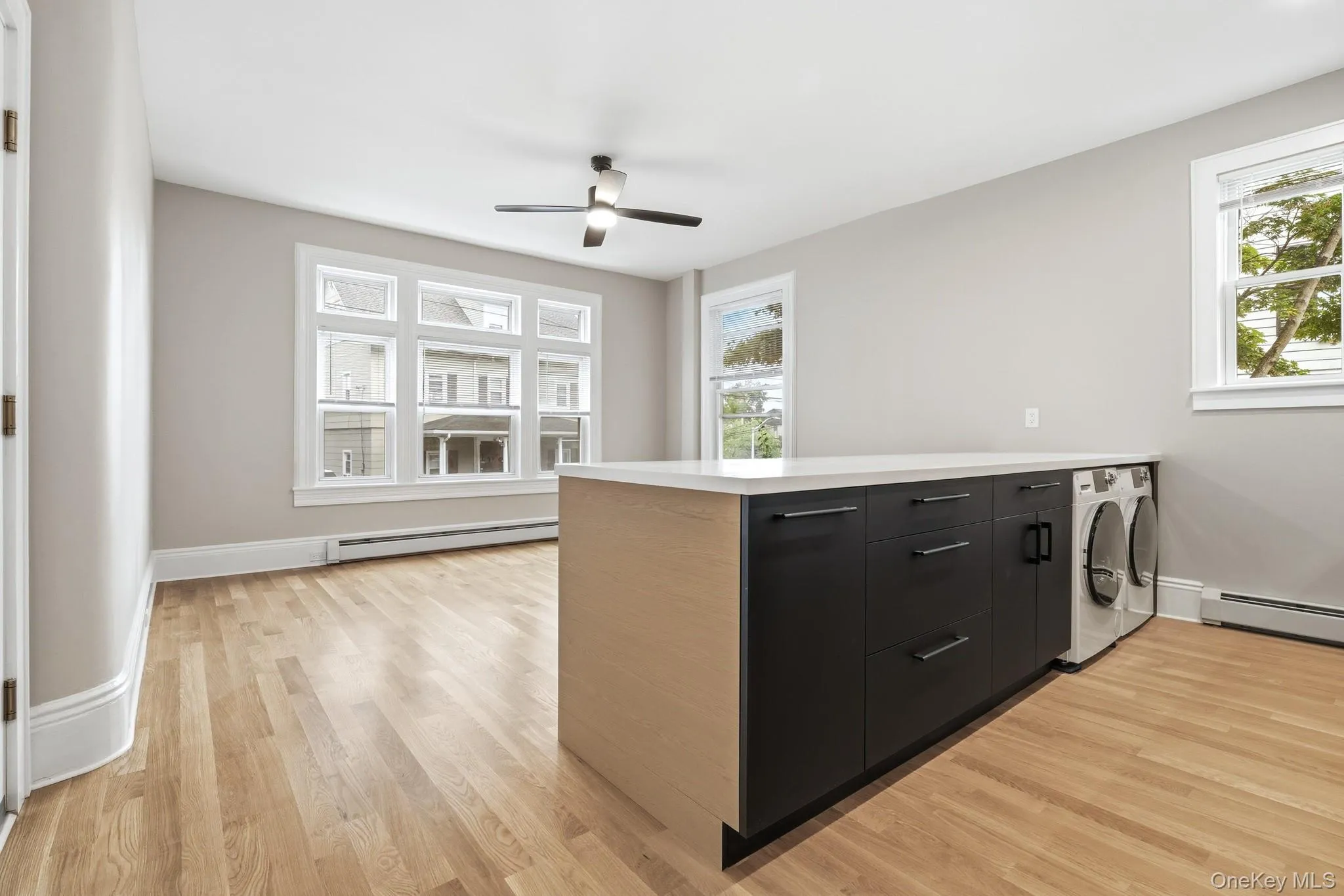 Contemporary kitchen featuring two-tone cabinetry, stainless steel appliances, white countertops, chef's sink, and light wood-finish flooring. Contemporary kitchen featuring two-tone cabinetry, stainless steel appliances, white countertops, chef's sink, and light wood-finish flooring.