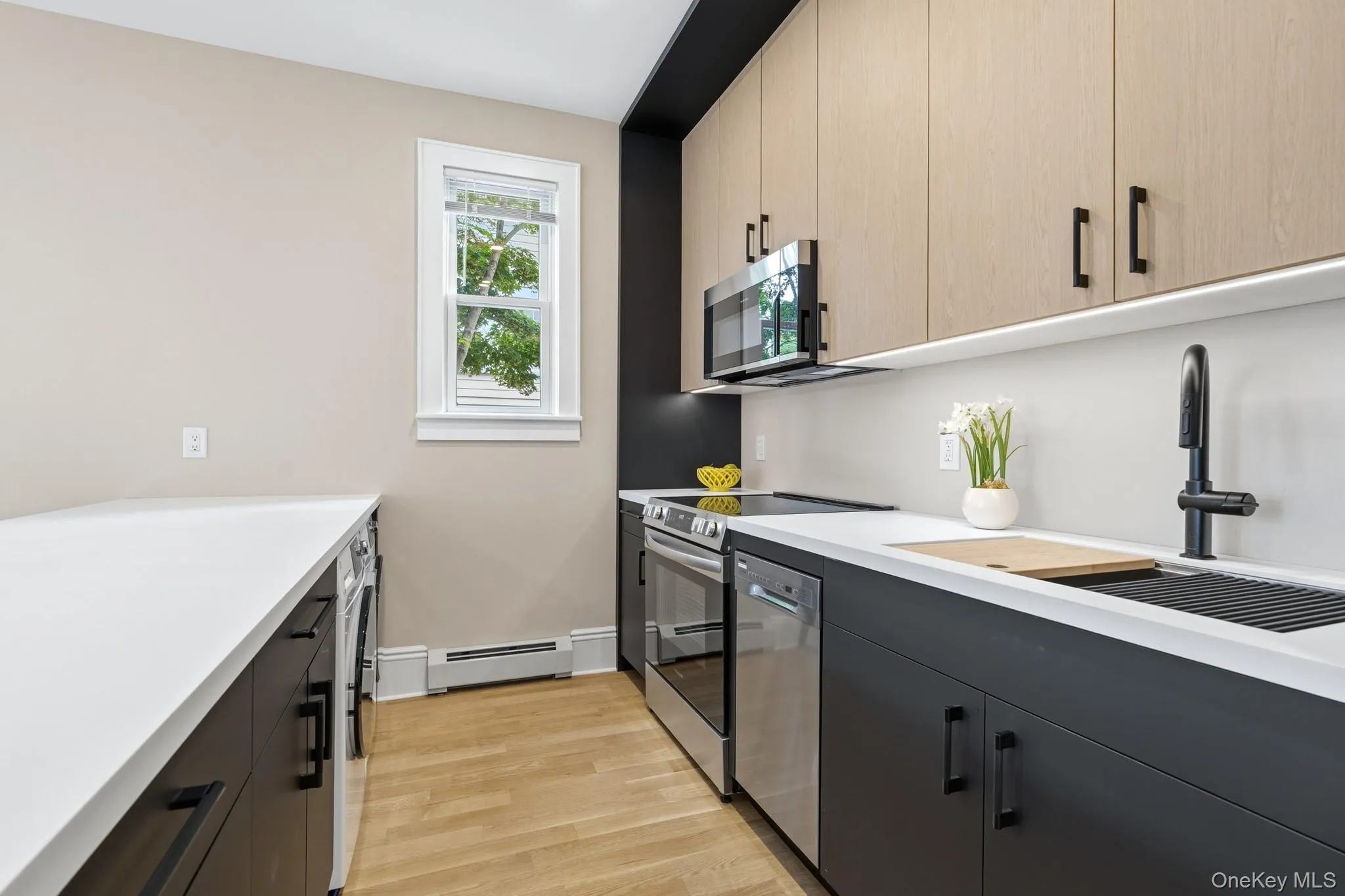 Contemporary kitchen featuring two-tone cabinetry, stainless steel appliances, white countertops, chef's sink, and light wood-finish flooring. Contemporary kitchen featuring two-tone cabinetry, stainless steel appliances, white countertops, chef's sink, and light wood-finish flooring.