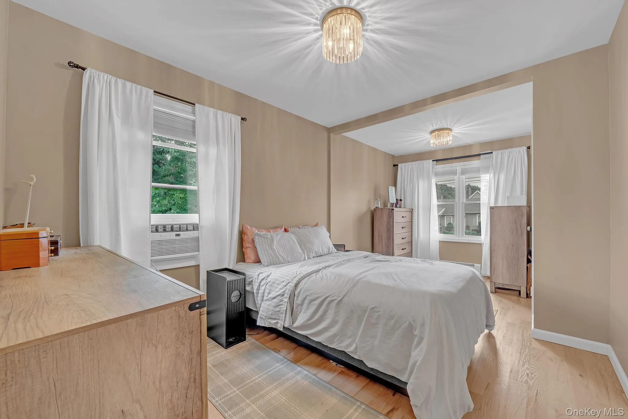 Hardwood-style flooring throughout, featuring a window with an integrated air conditioning unit, neutral-toned walls, and a contemporary ceiling light fixture Hardwood-style flooring throughout, featuring a window with an integrated air conditioning unit, neutral-toned walls, and a contemporary ceiling light fixture