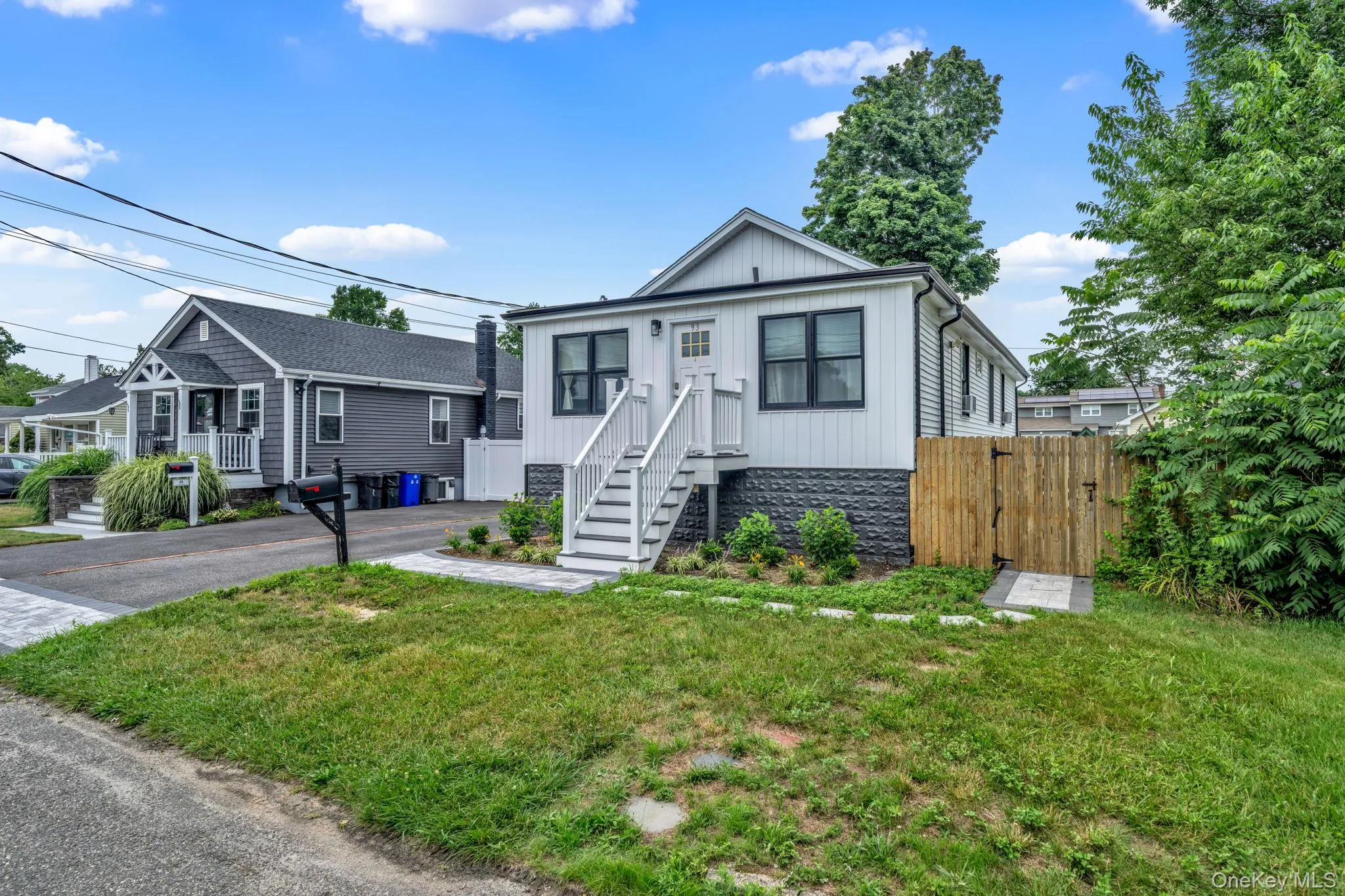 Modern exterior featuring white siding, black-trimmed windows, a prominent front staircase, and a wood-paneled privacy fence Modern exterior featuring white siding, black-trimmed windows, a prominent front staircase, and a wood-paneled privacy fence