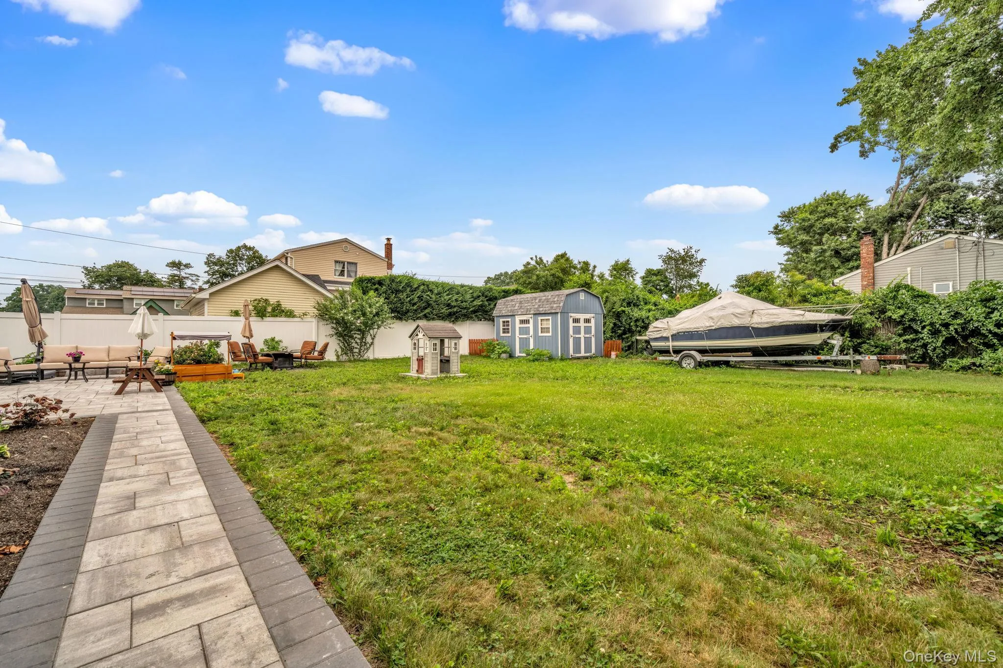 Expansive backyard featuring a large paved patio, a stone paver pathway, lush green lawn, and a detached storage shed Expansive backyard featuring a large paved patio, a stone paver pathway, lush green lawn, and a detached storage shed