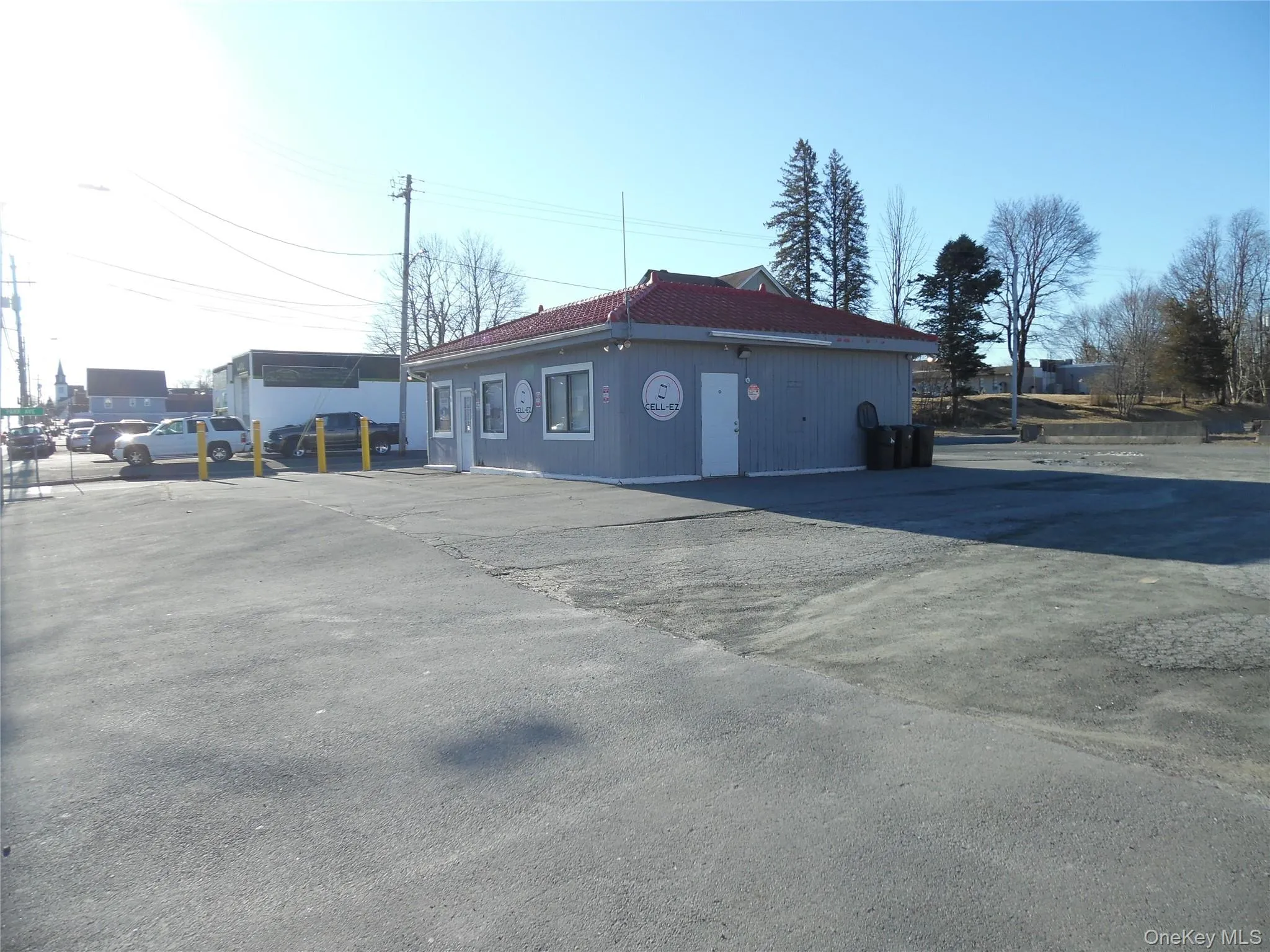 Commercial building featuring a light gray exterior, red tile roof, multiple windows, and a dedicated parking area Commercial building featuring a light gray exterior, red tile roof, multiple windows, and a dedicated parking area