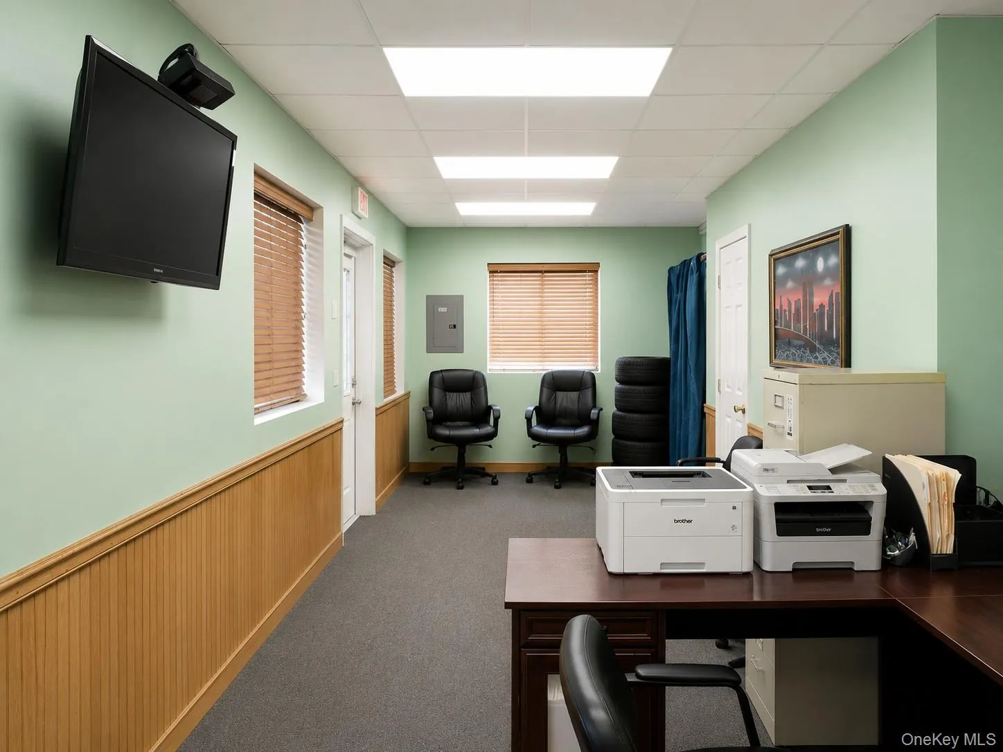 Corridor featuring wainscoting, recessed lighting, wall-mounted display, and multiple windows with blinds Corridor featuring wainscoting, recessed lighting, wall-mounted display, and multiple windows with blinds