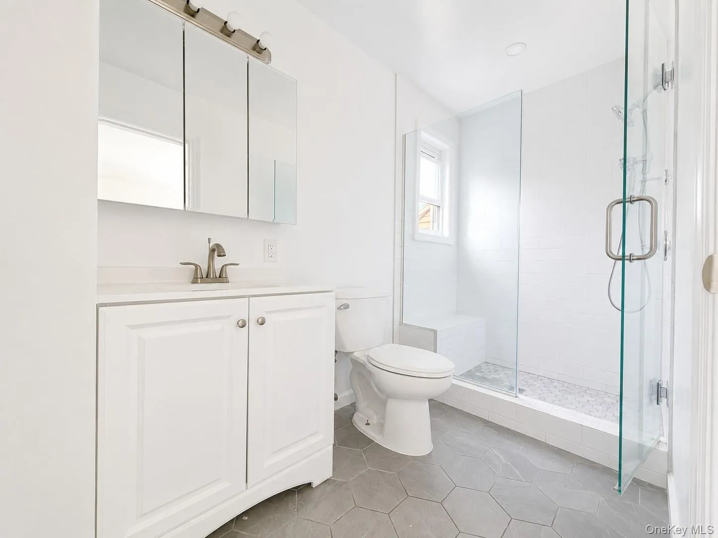 Bathroom featuring a glass-enclosed shower with a built-in bench, hexagon tile flooring, a white vanity with a countertop, a mirrored medicine cabinet, and a window Bathroom featuring a glass-enclosed shower with a built-in bench, hexagon tile flooring, a white vanity with a countertop, a mirrored medicine cabinet, and a window