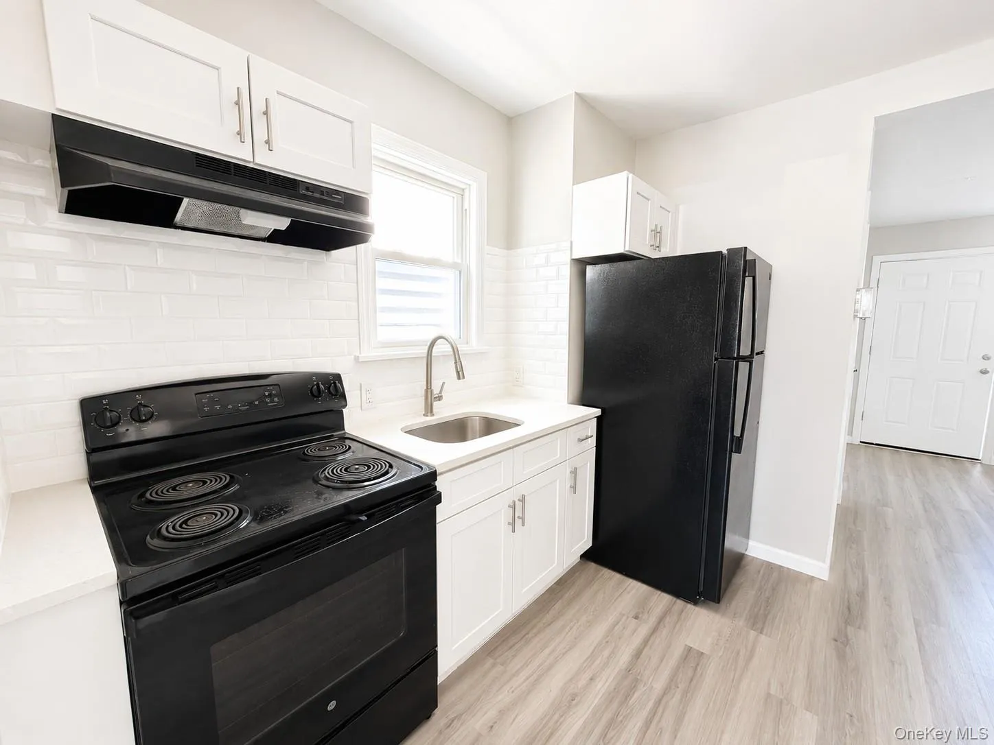 Kitchen featuring white shaker cabinetry, white subway tile backsplash, white countertops, and wood-finish flooring Kitchen featuring white shaker cabinetry, white subway tile backsplash, white countertops, and wood-finish flooring
