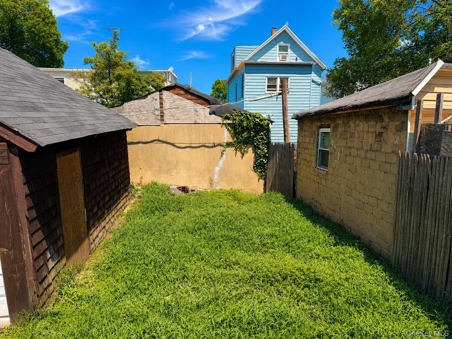 Grassed yard area featuring a shingled shed, privacy fencing, and a stucco wall Grassed yard area featuring a shingled shed, privacy fencing, and a stucco wall