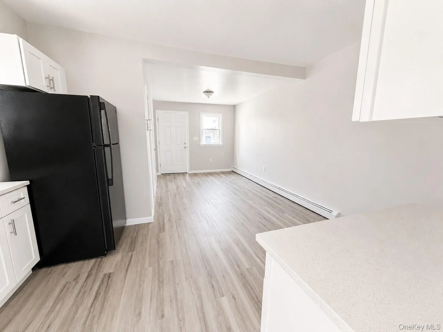 Kitchen area featuring white cabinetry, light-toned countertops, a black refrigerator, and wood-finish flooring Kitchen area featuring white cabinetry, light-toned countertops, a black refrigerator, and wood-finish flooring