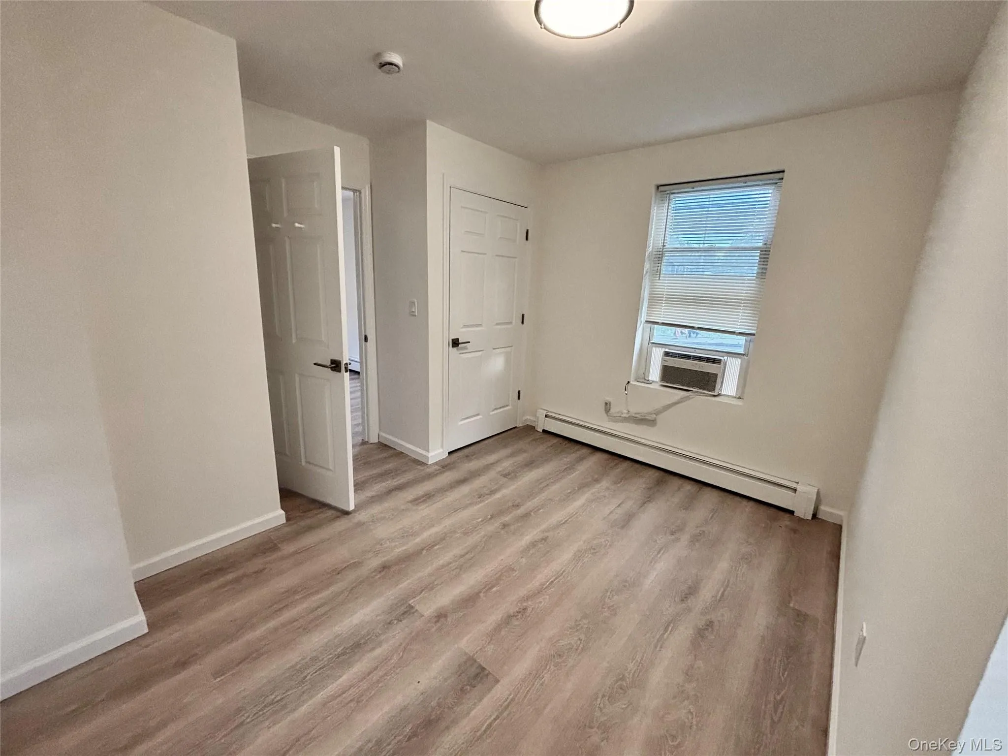 Unfurnished bedroom featuring a baseboard radiator, light wood-style floors, baseboards, and cooling unit Unfurnished bedroom featuring a baseboard radiator, light wood-style floors, baseboards, and cooling unit