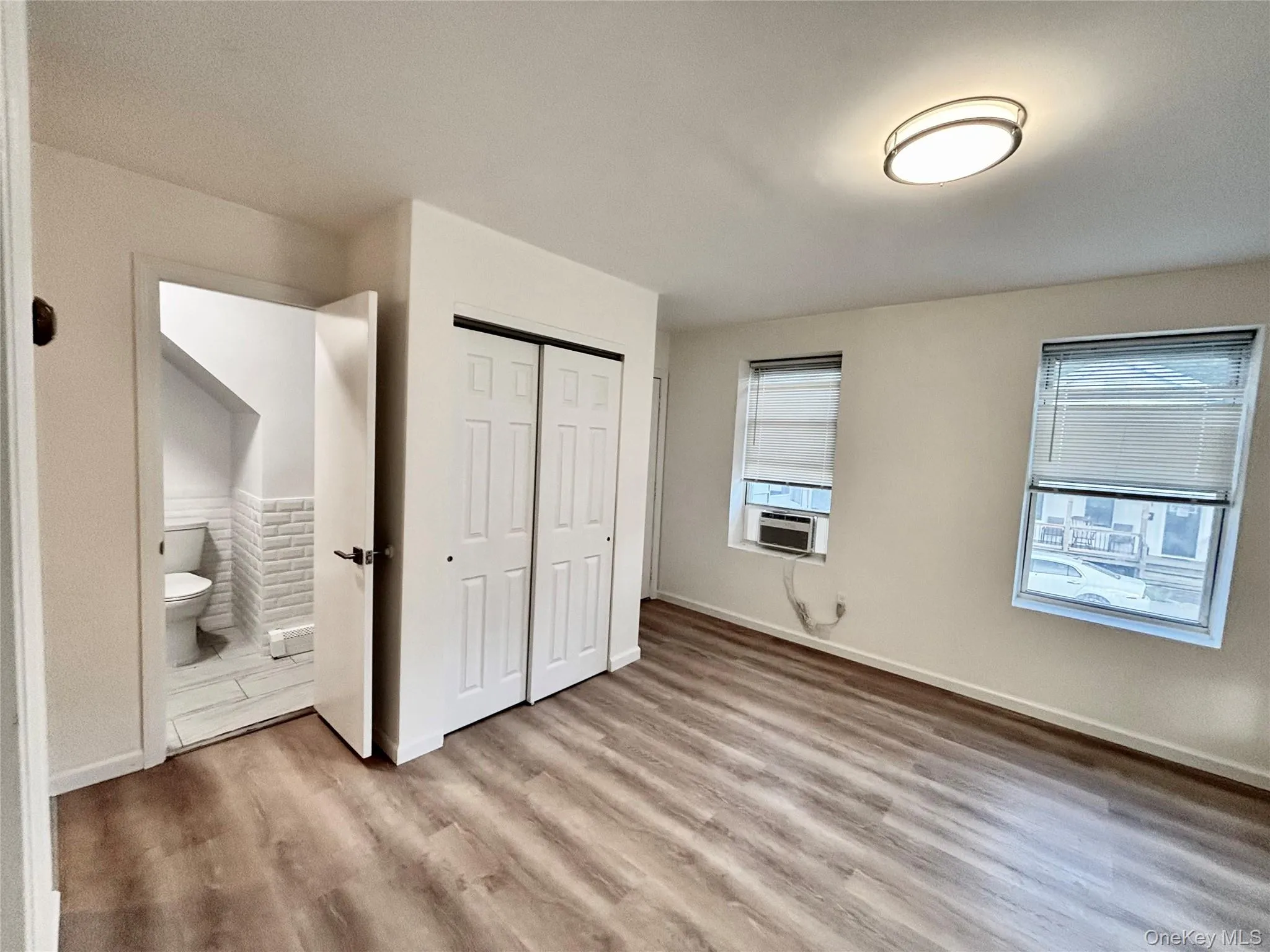 Unfurnished bedroom with wood finished floors, a closet, ensuite bath, cooling unit, and baseboards Unfurnished bedroom with wood finished floors, a closet, ensuite bath, cooling unit, and baseboards