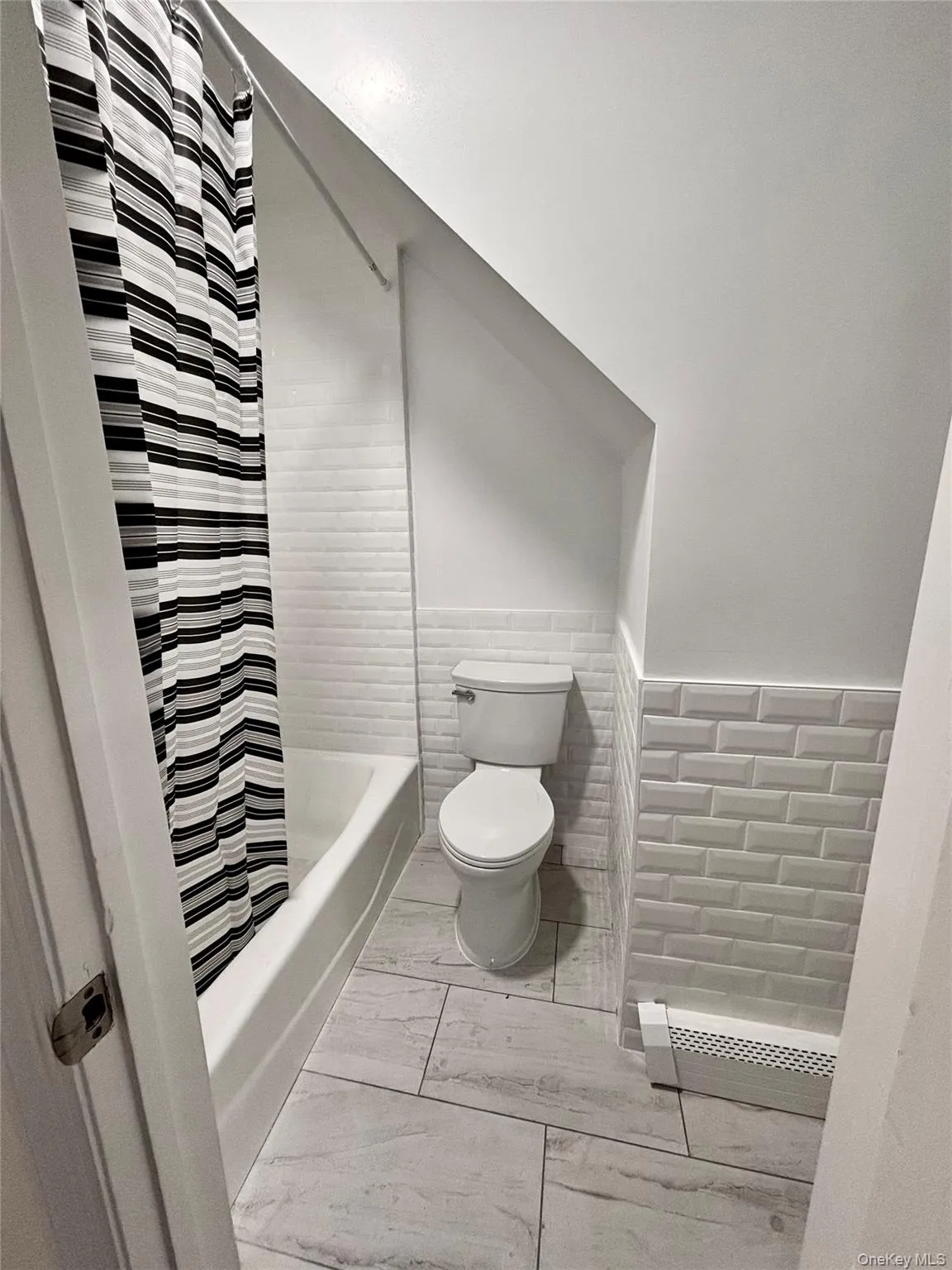 Bathroom featuring toilet, shower / bathtub combination with curtain, wainscoting, and marble look tile flooring Bathroom featuring toilet, shower / bathtub combination with curtain, wainscoting, and marble look tile flooring