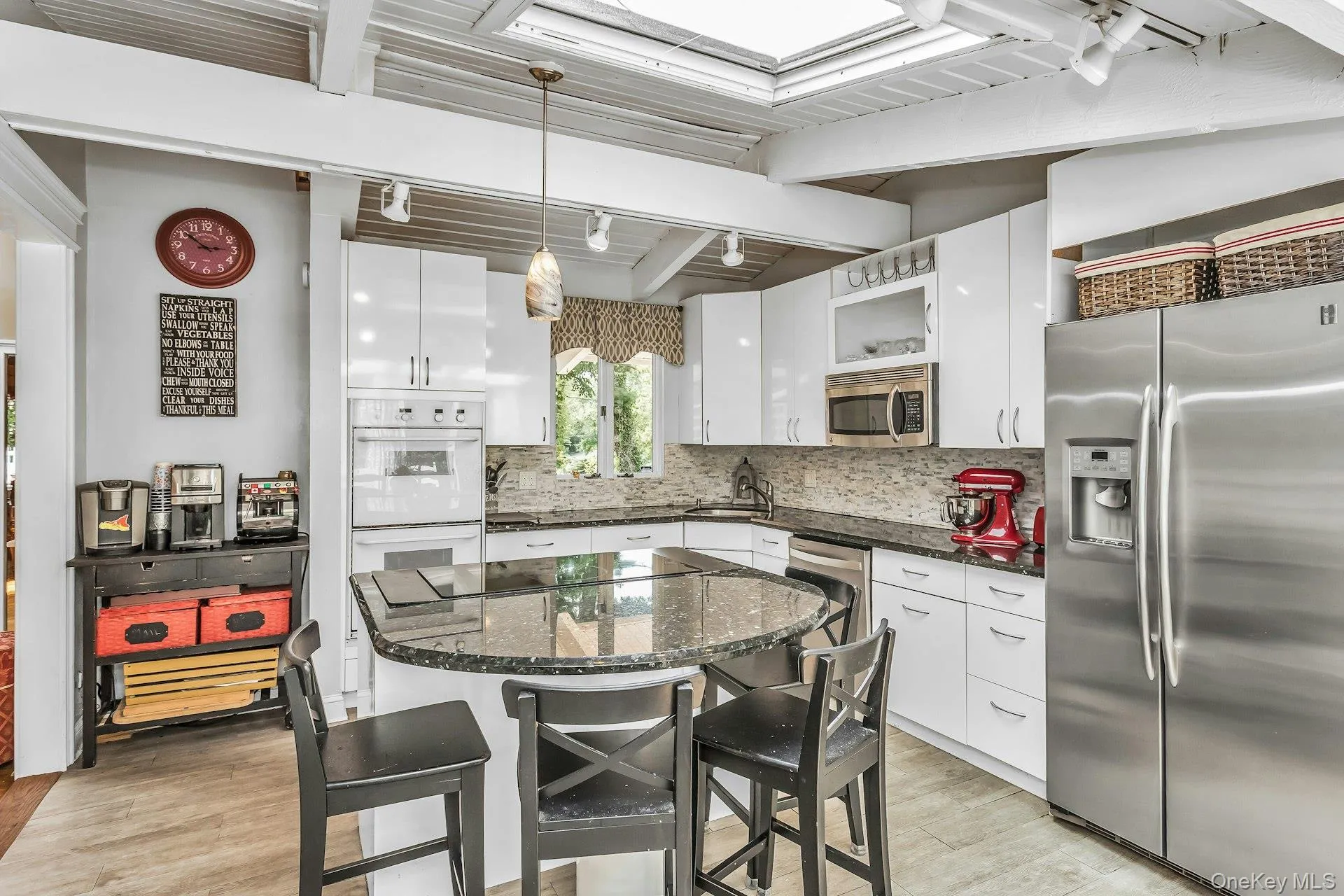 Kitchen featuring exposed wood beam ceilings with skylights, white cabinetry, dark granite countertops, stainless steel appliances, coffee bar and a central island with breakfast seating Kitchen featuring exposed wood beam ceilings with skylights, white cabinetry, dark granite countertops, stainless steel appliances, coffee bar and a central island with breakfast seating