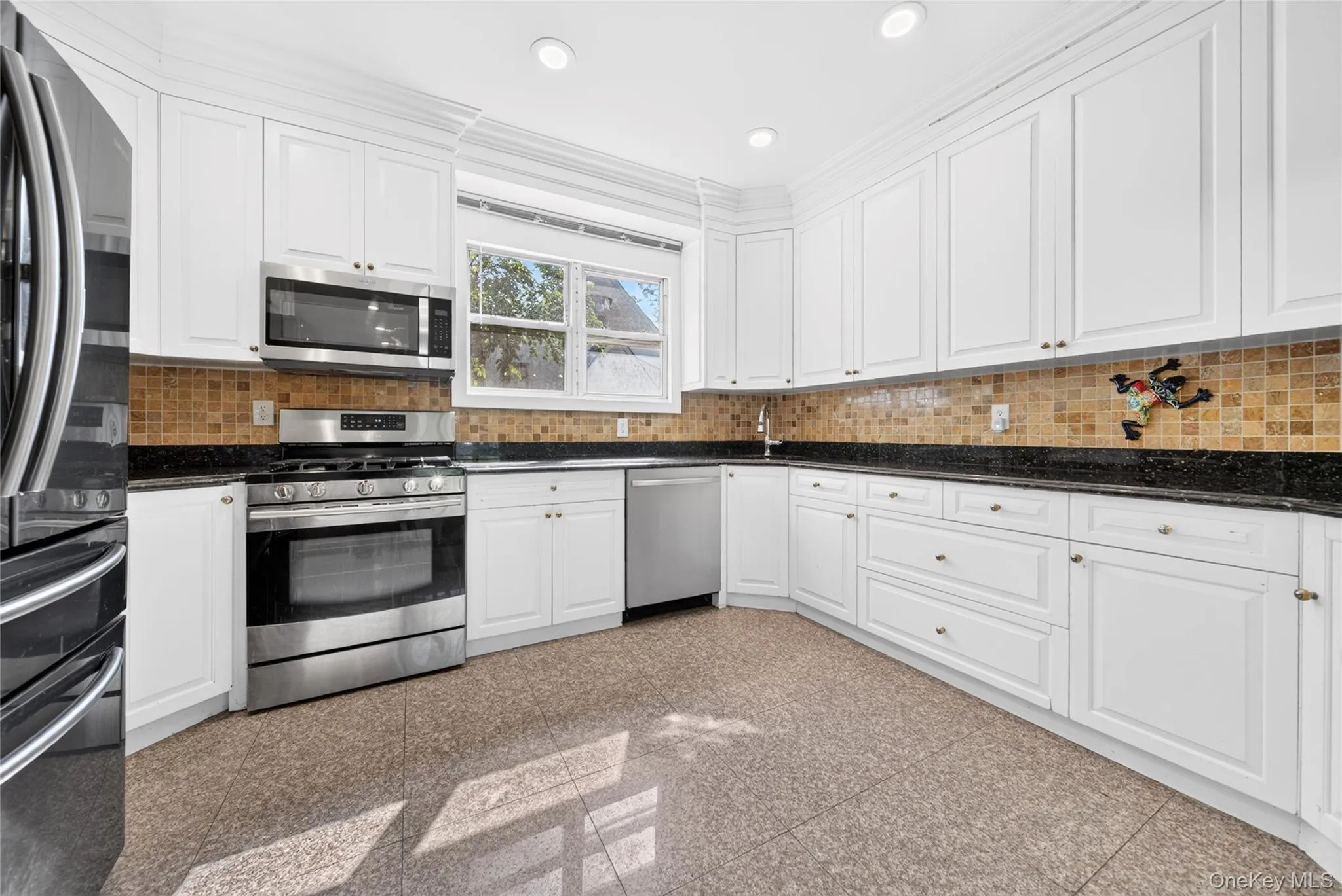 Kitchen featuring extensive white cabinetry, stainless steel appliances, dark countertops, a tiled backsplash, and recessed lighting Kitchen featuring extensive white cabinetry, stainless steel appliances, dark countertops, a tiled backsplash, and recessed lighting