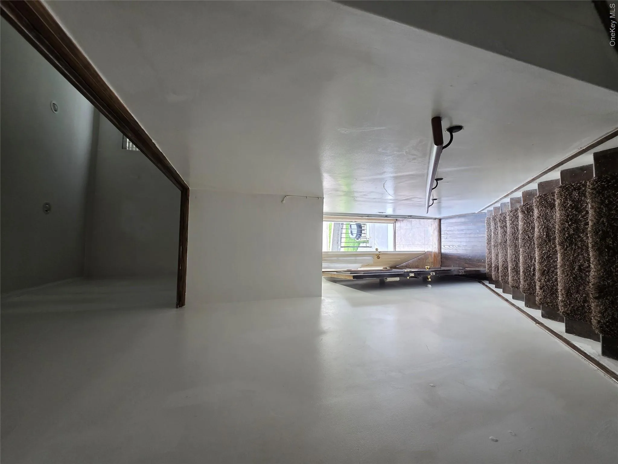 Carpeted staircase featuring a metal handrail, leading to an entryway with a visible door and wood-finish flooring Carpeted staircase featuring a metal handrail, leading to an entryway with a visible door and wood-finish flooring