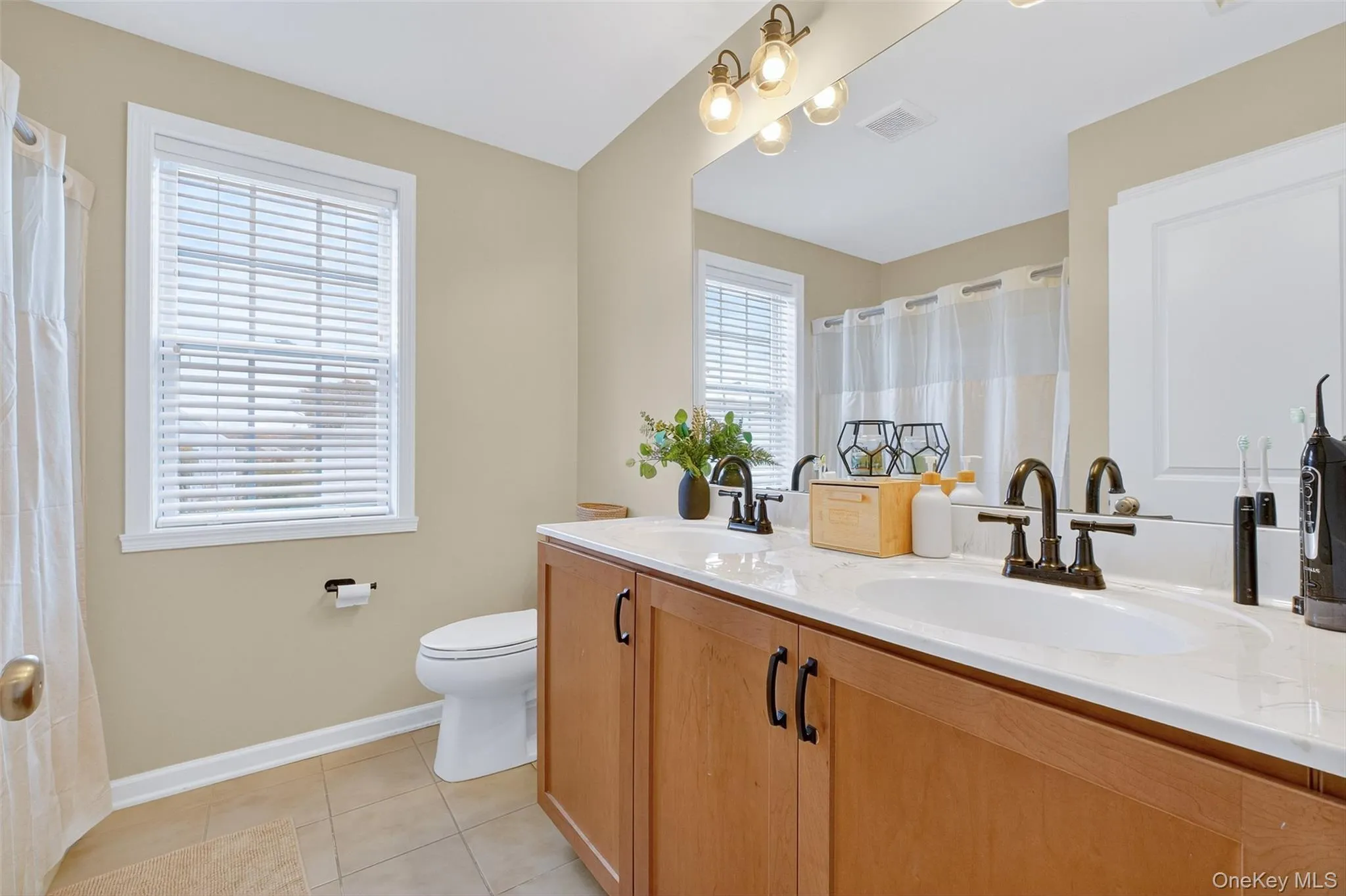 Full bathroom featuring double vanity, light tile patterned floors, and a shower Full bathroom featuring double vanity, light tile patterned floors, and a shower