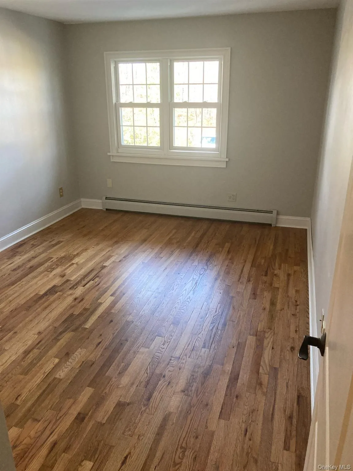 Unfurnished room with a baseboard heating unit and wood finished floors Unfurnished room with a baseboard heating unit and wood finished floors