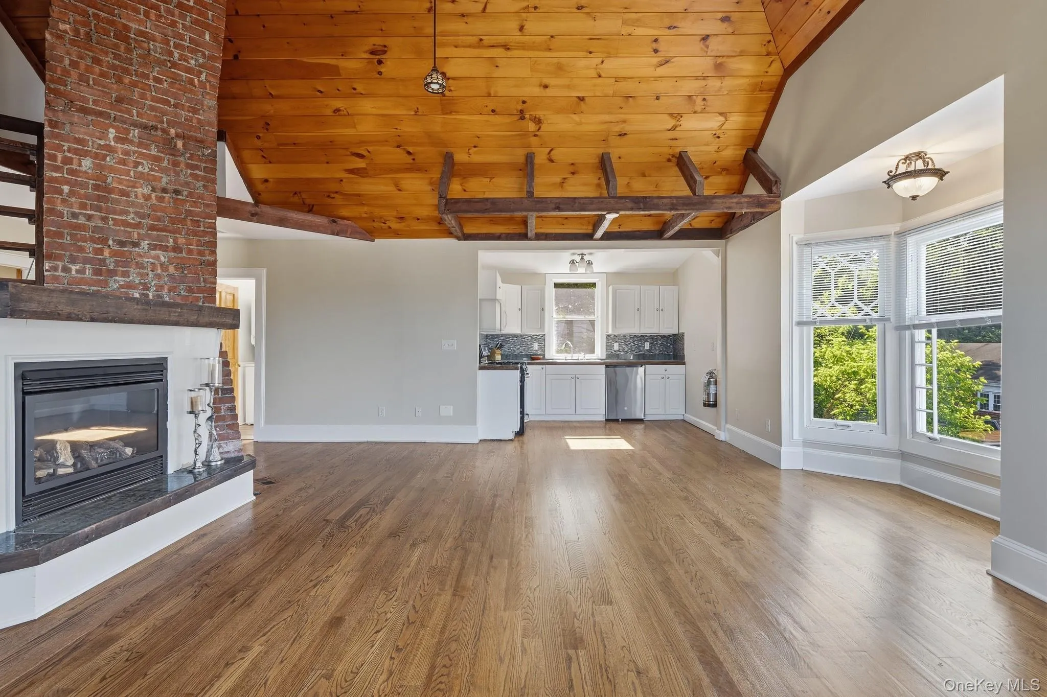 The bright and airy living room features vaulted wood-plank ceiling with exposed beams, big bright windows from every angle, bay windows, working fireplace, and original hardwood flooring. The bright and airy living room features vaulted wood-plank ceiling with exposed beams, big bright windows from every angle, bay windows, working fireplace, and original hardwood flooring.