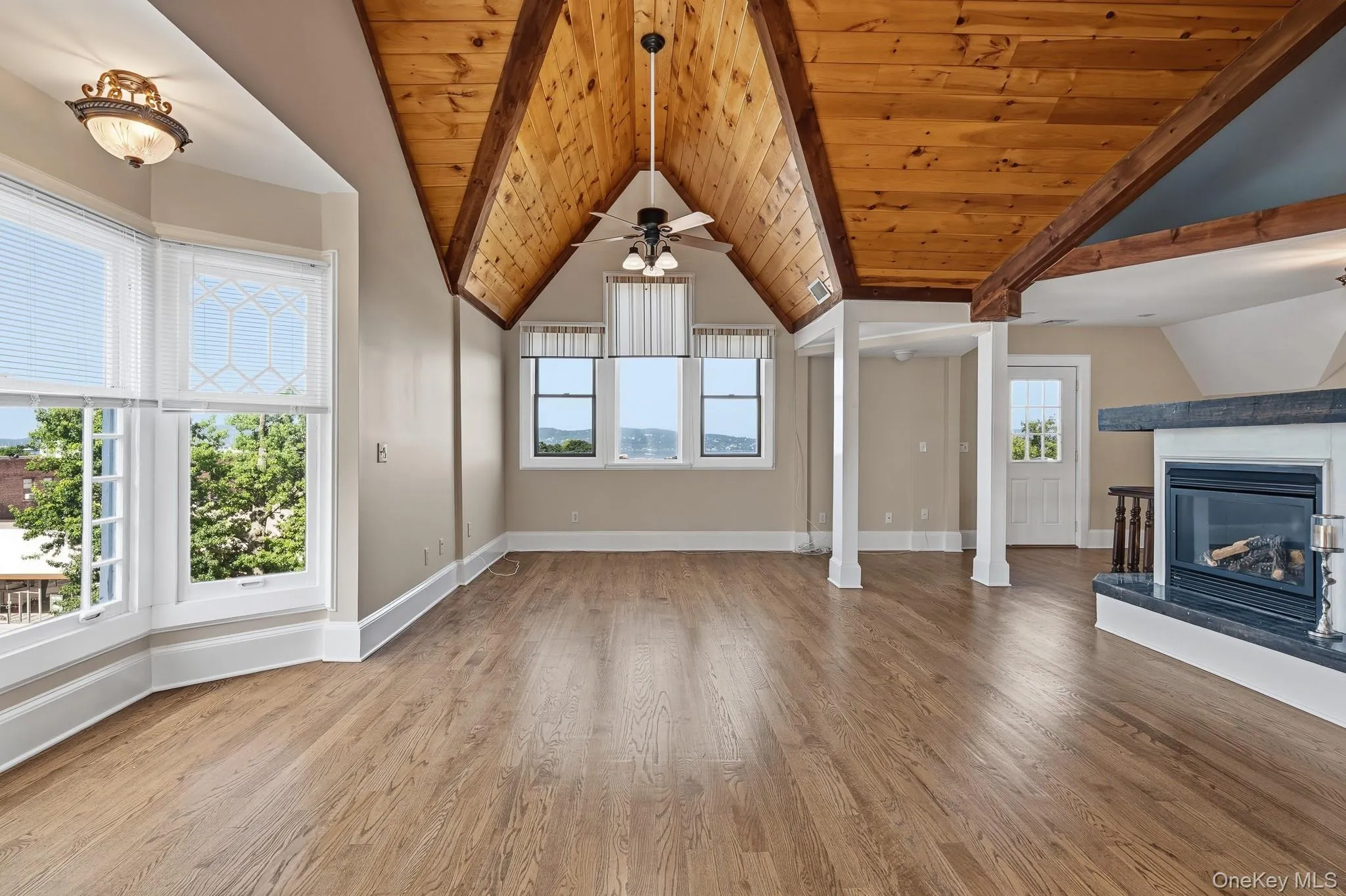 The bright and airy living room features vaulted wood-plank ceiling with exposed beams, big bright windows from every angle, bay windows, working fireplace, and original hardwood flooring. The bright and airy living room features vaulted wood-plank ceiling with exposed beams, big bright windows from every angle, bay windows, working fireplace, and original hardwood flooring.