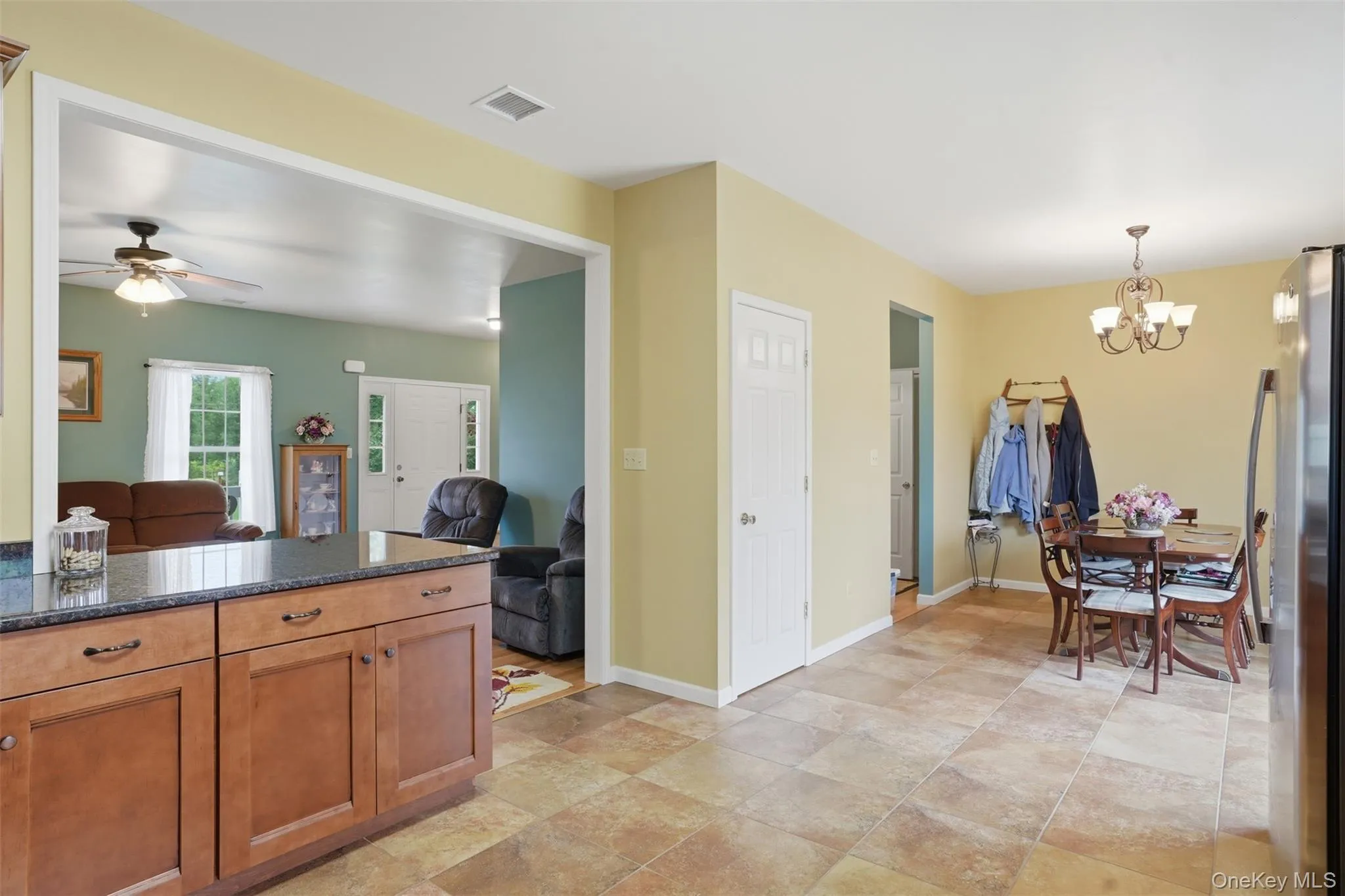 Open-concept kitchen and dining area featuring wood cabinetry, dark stone countertops, and tile flooring Open-concept kitchen and dining area featuring wood cabinetry, dark stone countertops, and tile flooring