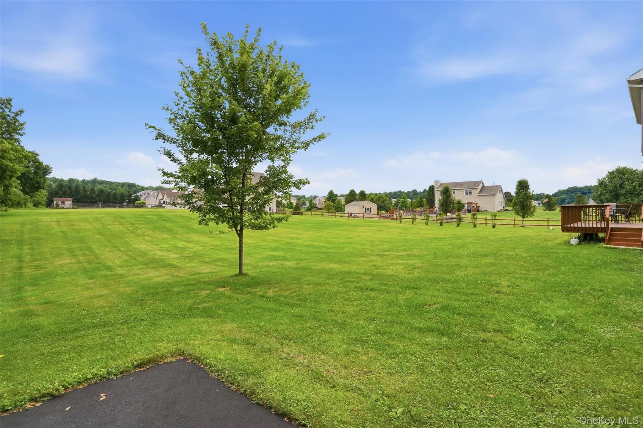 Expansive green space featuring a mature tree, natural wood fencing, and a multi-level wood deck Expansive green space featuring a mature tree, natural wood fencing, and a multi-level wood deck