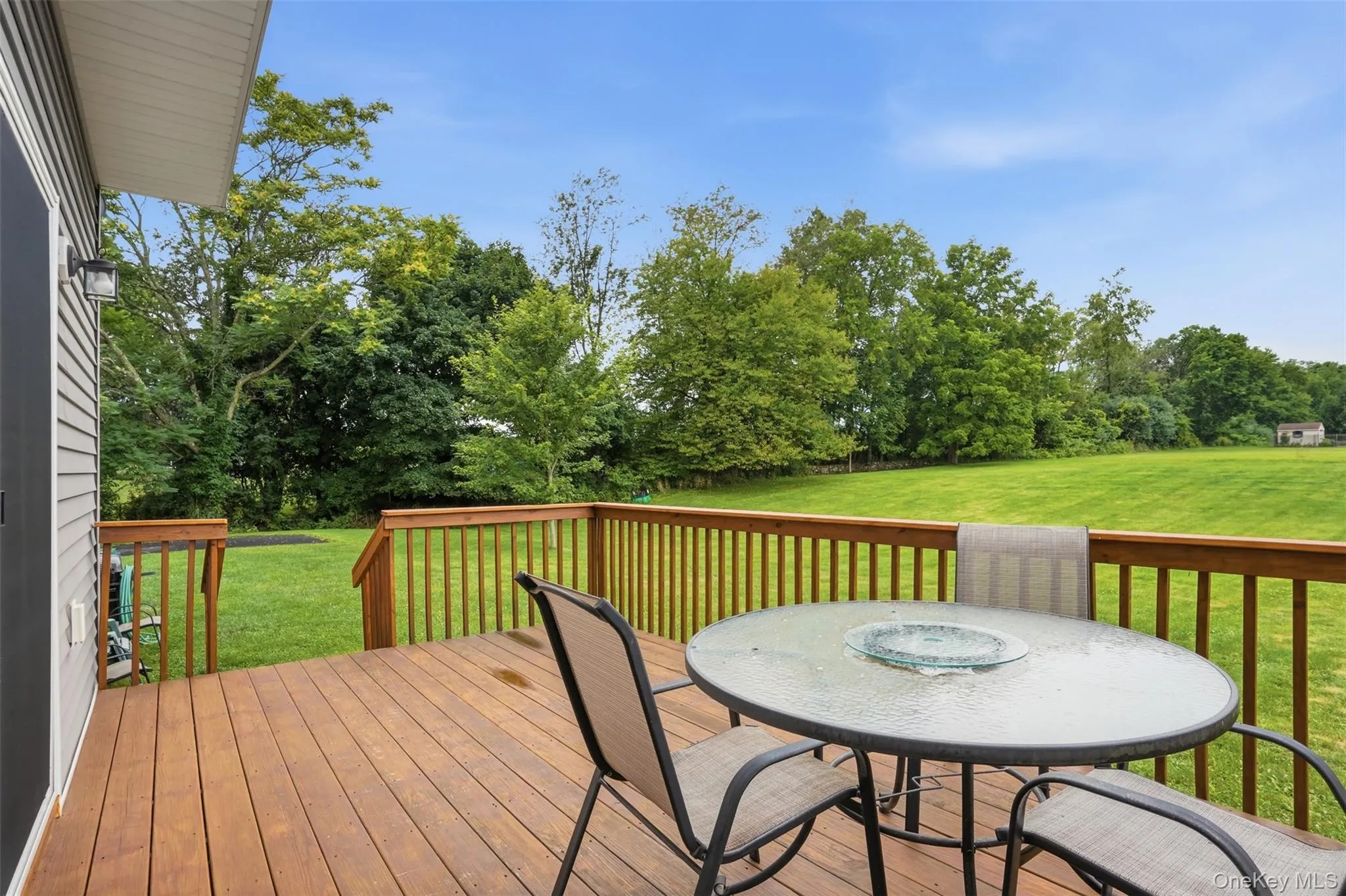 Spacious wood deck with wood railings, overlooking an expansive green lawn and mature trees Spacious wood deck with wood railings, overlooking an expansive green lawn and mature trees