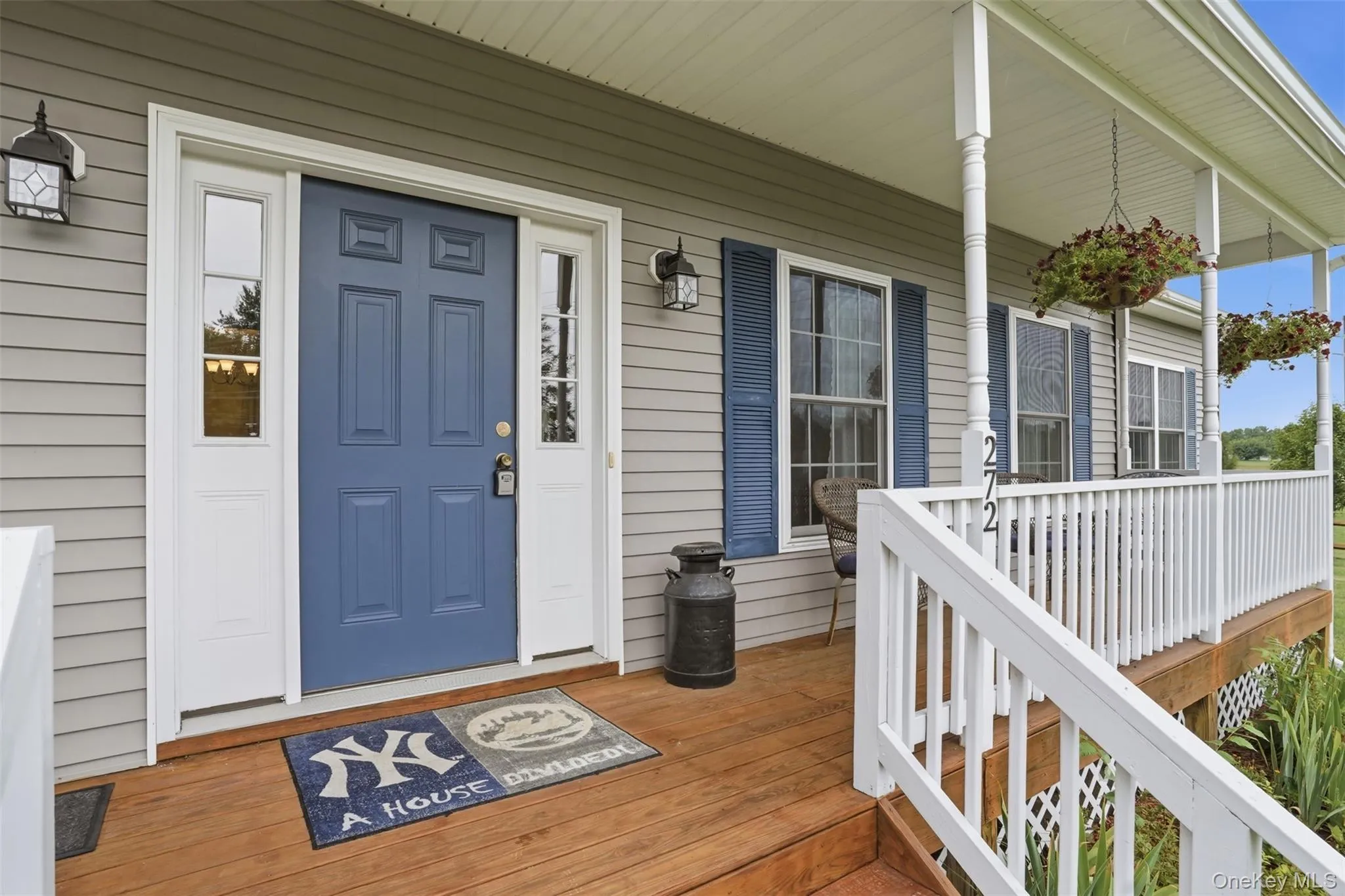 Exterior featuring light gray siding, a blue paneled entry door with sidelights, a wood-finish porch deck, white railings, and blue window shutters Exterior featuring light gray siding, a blue paneled entry door with sidelights, a wood-finish porch deck, white railings, and blue window shutters