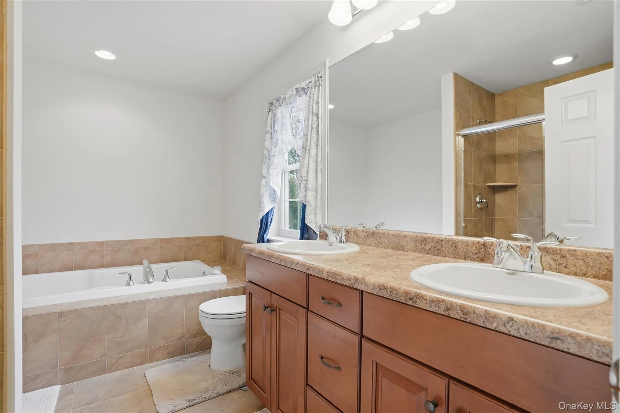 Bathroom featuring a dual vanity with laminate countertop, integrated sinks, and wood-finish cabinetry Bathroom featuring a dual vanity with laminate countertop, integrated sinks, and wood-finish cabinetry
