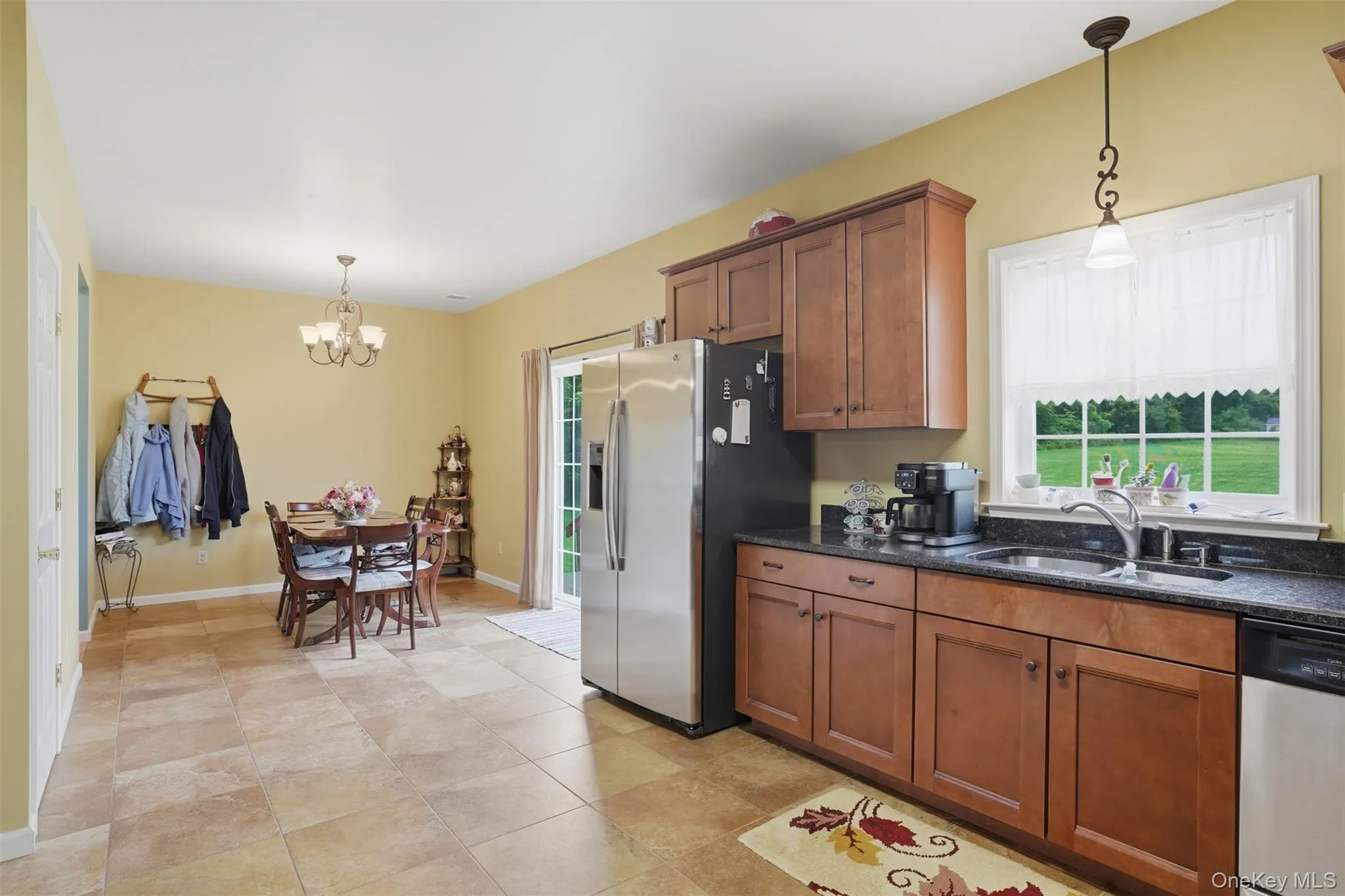 Kitchen featuring wood-finish cabinetry, dark countertops, a stainless steel refrigerator, and tile flooring Kitchen featuring wood-finish cabinetry, dark countertops, a stainless steel refrigerator, and tile flooring