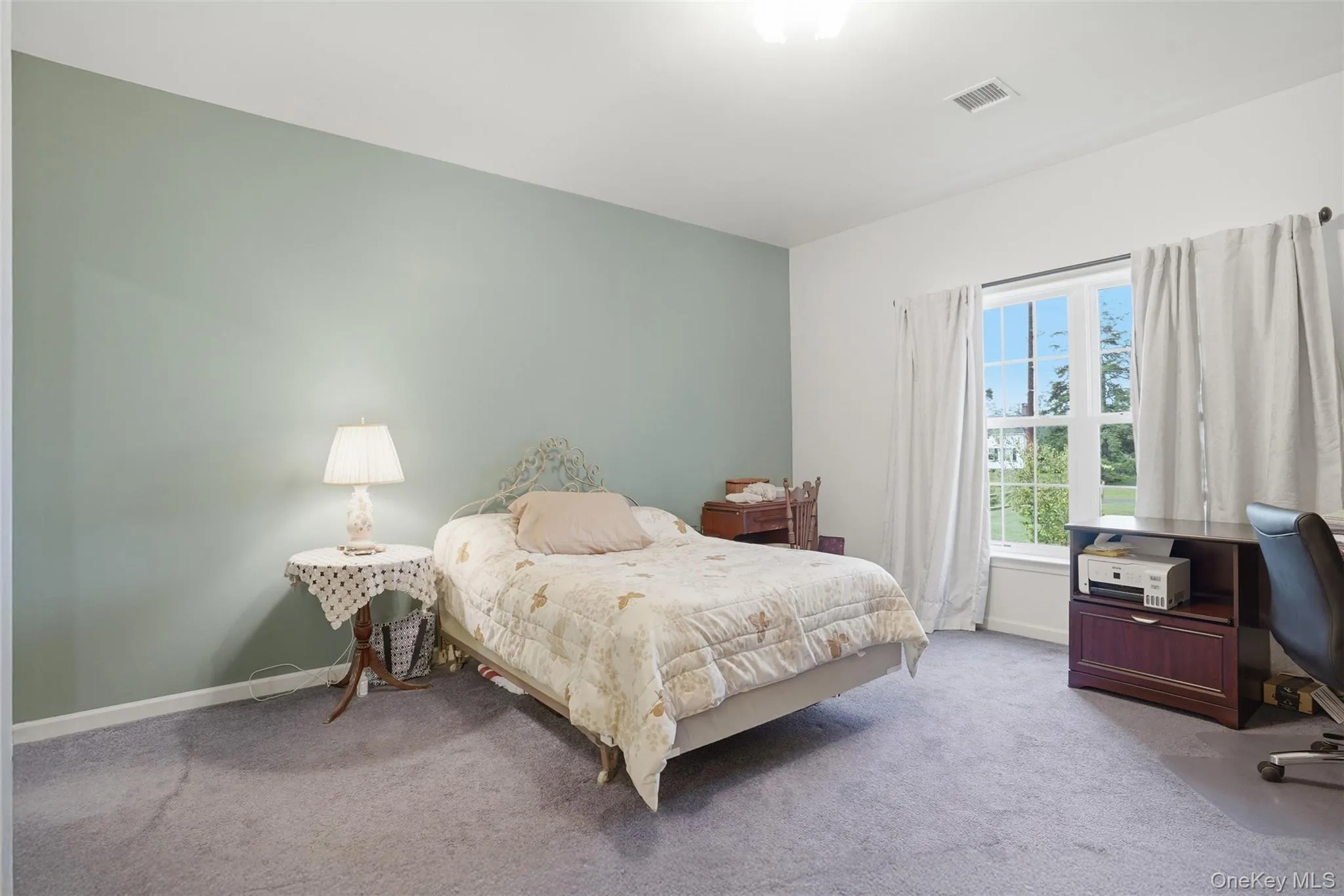 Bedroom featuring a single window with white trim, light green accent wall, light-colored carpeting, and white baseboards Bedroom featuring a single window with white trim, light green accent wall, light-colored carpeting, and white baseboards