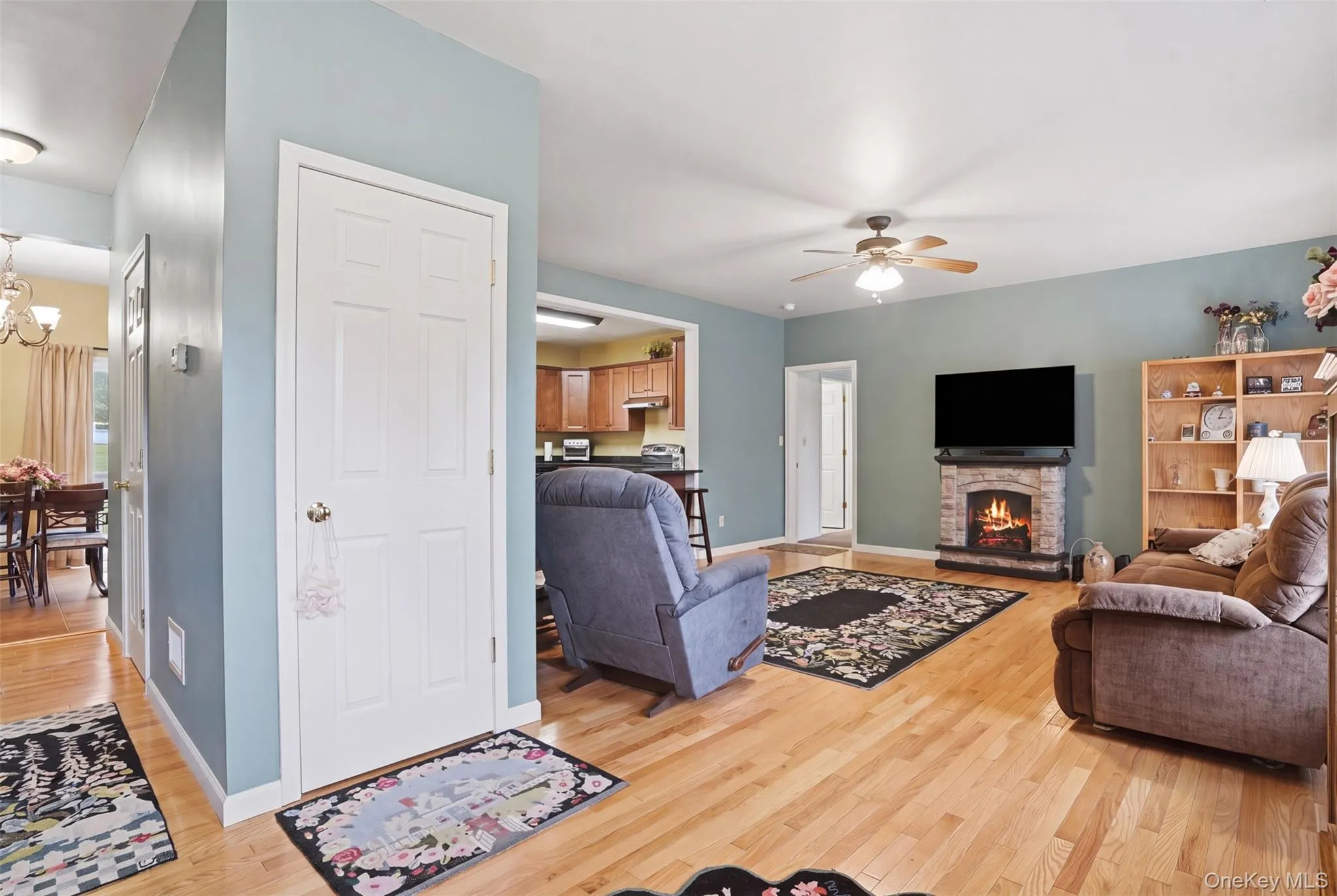 Living area featuring wood-finish flooring, a stone-look fireplace, and a ceiling fan with integrated lighting Living area featuring wood-finish flooring, a stone-look fireplace, and a ceiling fan with integrated lighting