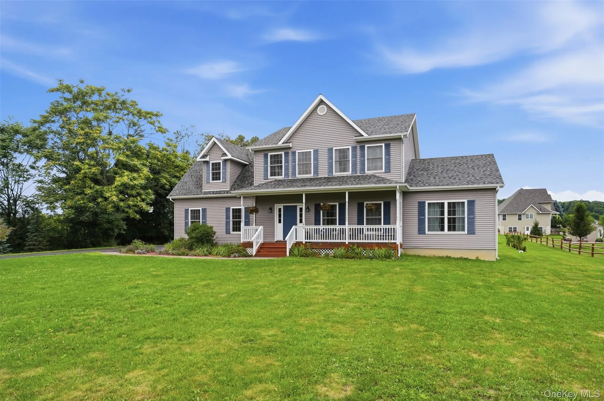 Expansive residential property featuring a gray siding exterior, a full-length front porch with white railings, a blue entry door, and blue window shutters Expansive residential property featuring a gray siding exterior, a full-length front porch with white railings, a blue entry door, and blue window shutters