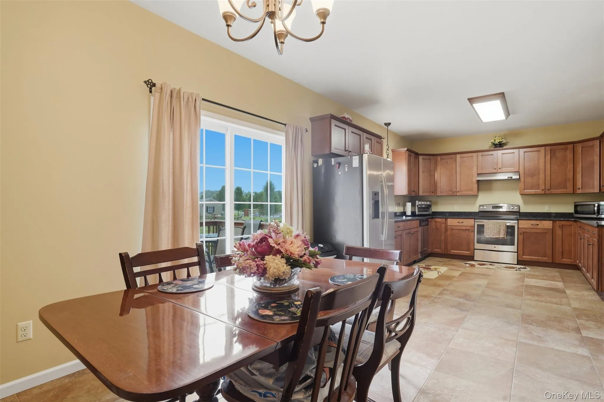 Open-concept kitchen and dining area featuring wood-finish cabinetry, stainless steel appliances, and a tiled floor Open-concept kitchen and dining area featuring wood-finish cabinetry, stainless steel appliances, and a tiled floor