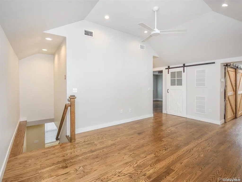 Unfurnished living room with a barn door, recessed lighting, wood finished floors, a ceiling fan, and high vaulted ceiling Unfurnished living room with a barn door, recessed lighting, wood finished floors, a ceiling fan, and high vaulted ceiling