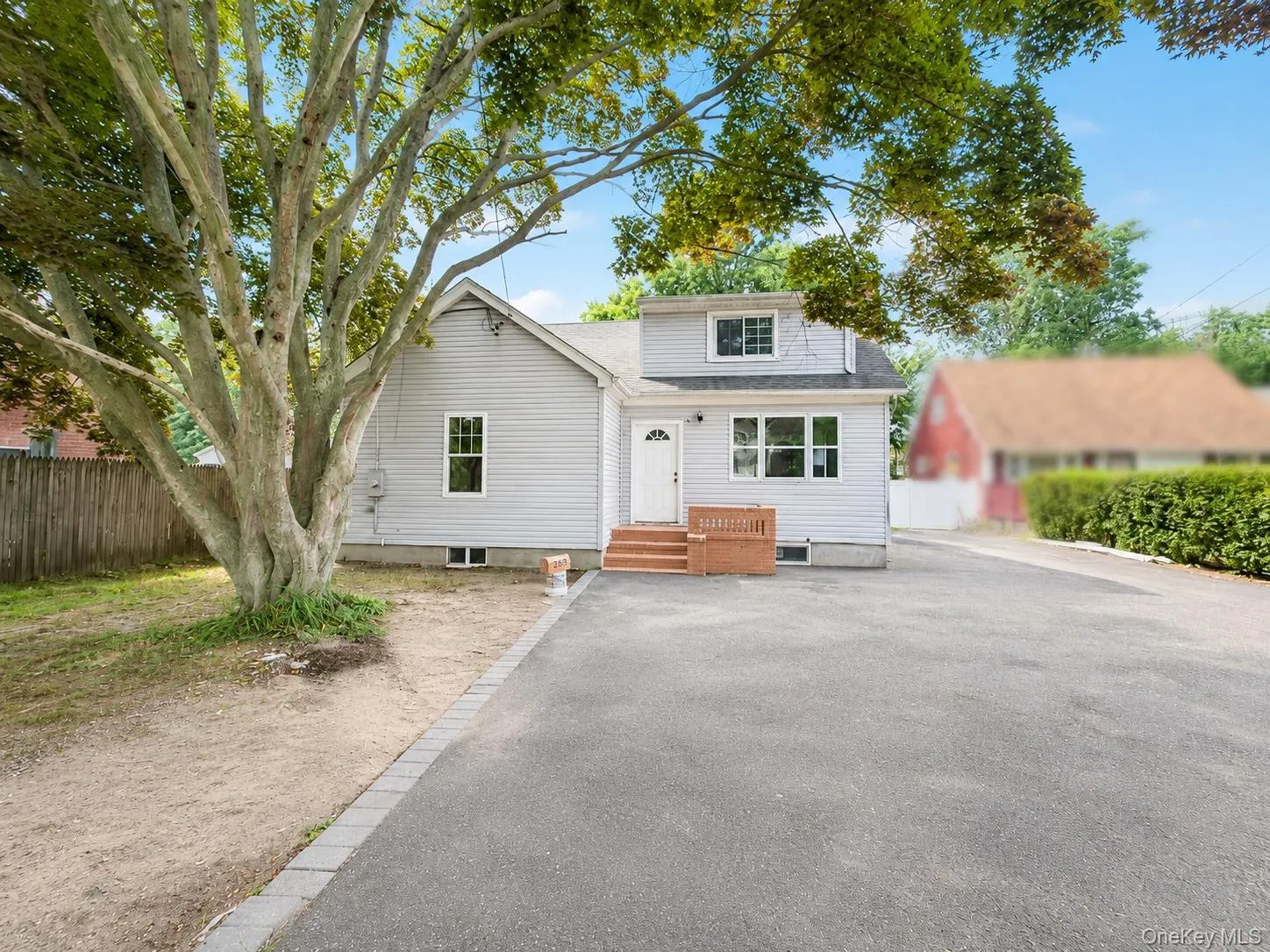 Light gray siding residence featuring a white front door, multi-pane windows, and a prominent mature tree Light gray siding residence featuring a white front door, multi-pane windows, and a prominent mature tree