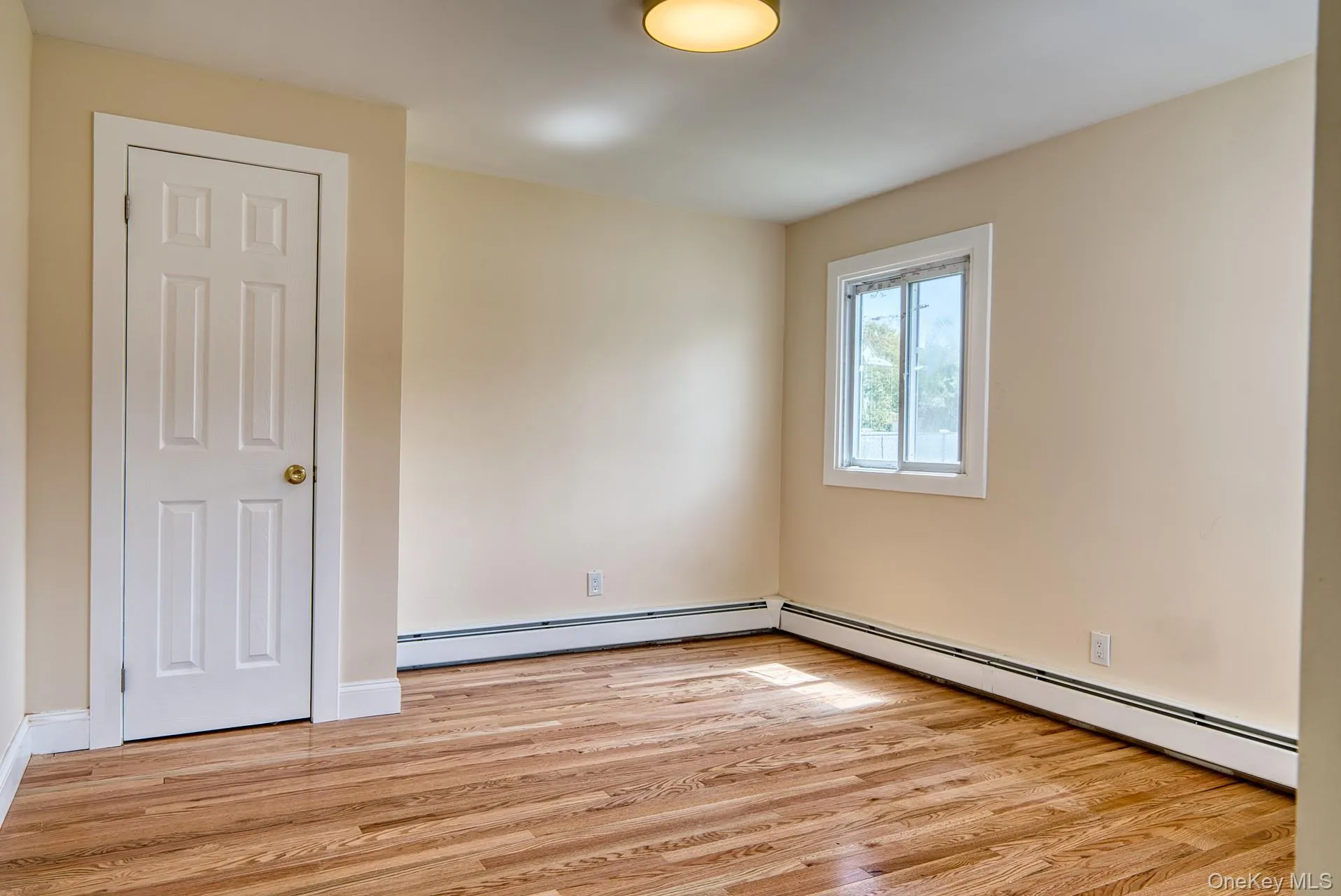 Empty room featuring light wood finished floors and a baseboard heating unit Empty room featuring light wood finished floors and a baseboard heating unit