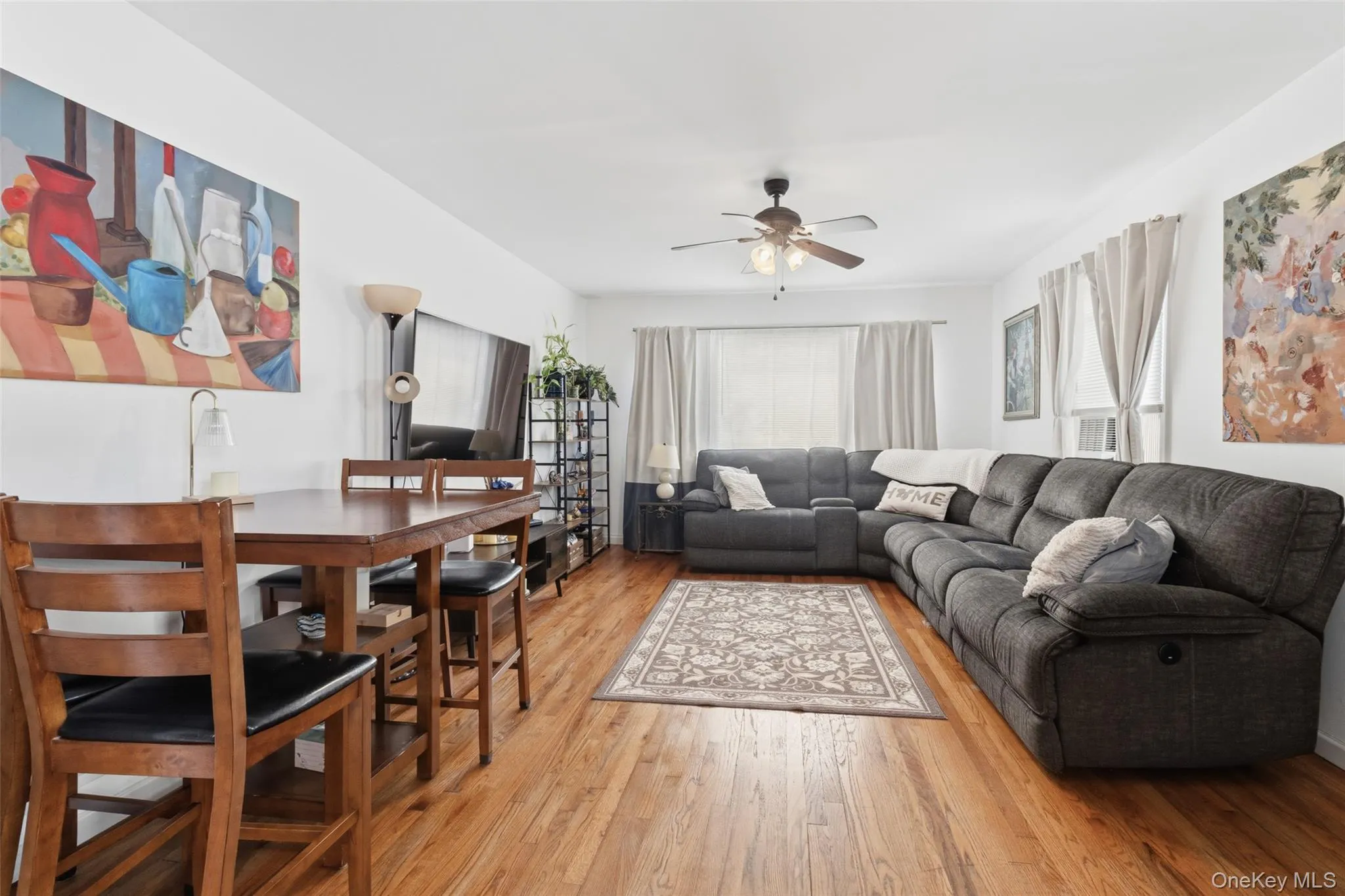 Open-concept living space with wood-finish flooring, a ceiling fan, and multiple windows Open-concept living space with wood-finish flooring, a ceiling fan, and multiple windows