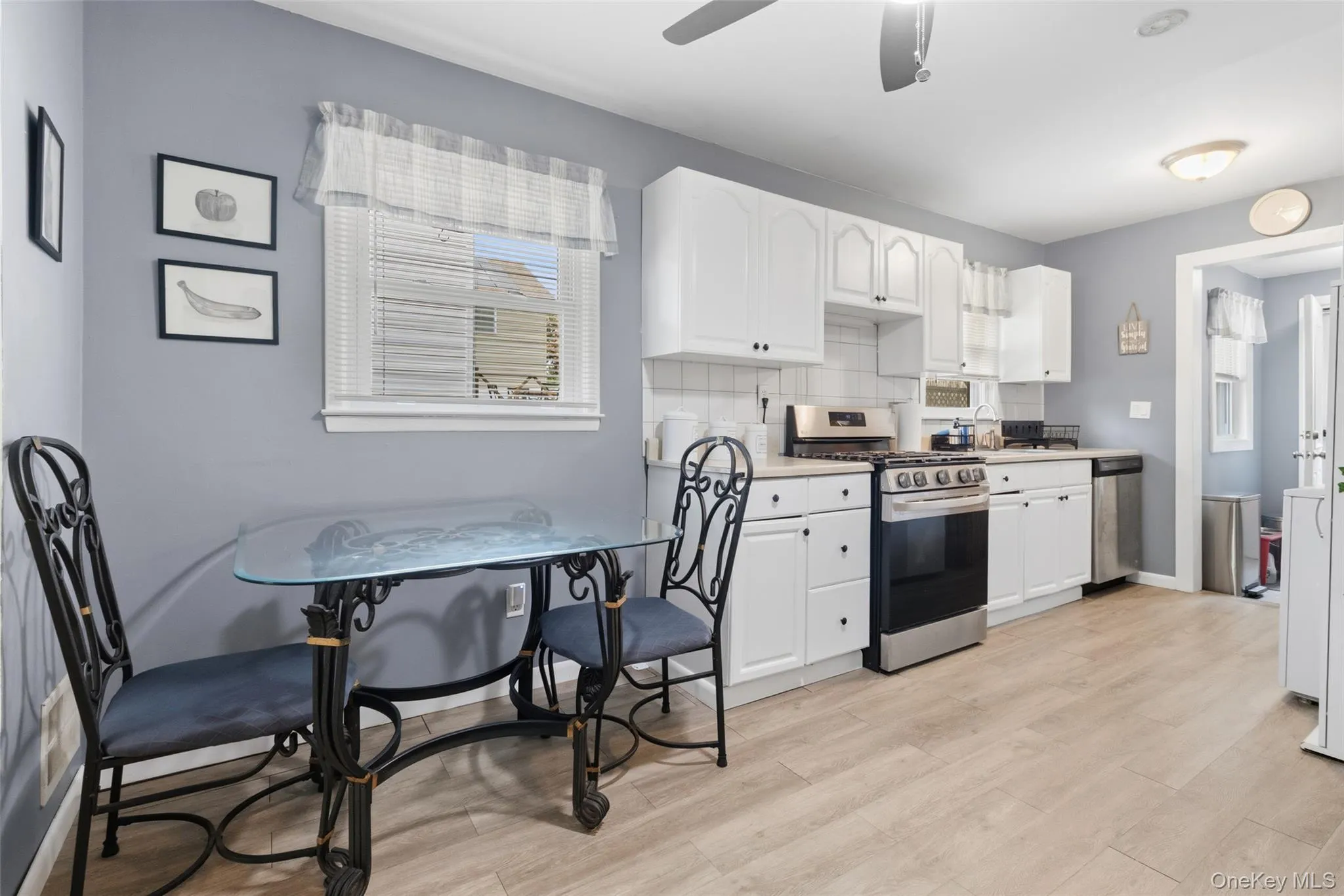 Kitchen featuring white cabinetry, stainless steel appliances, light wood-finish flooring, and a window with white blinds Kitchen featuring white cabinetry, stainless steel appliances, light wood-finish flooring, and a window with white blinds