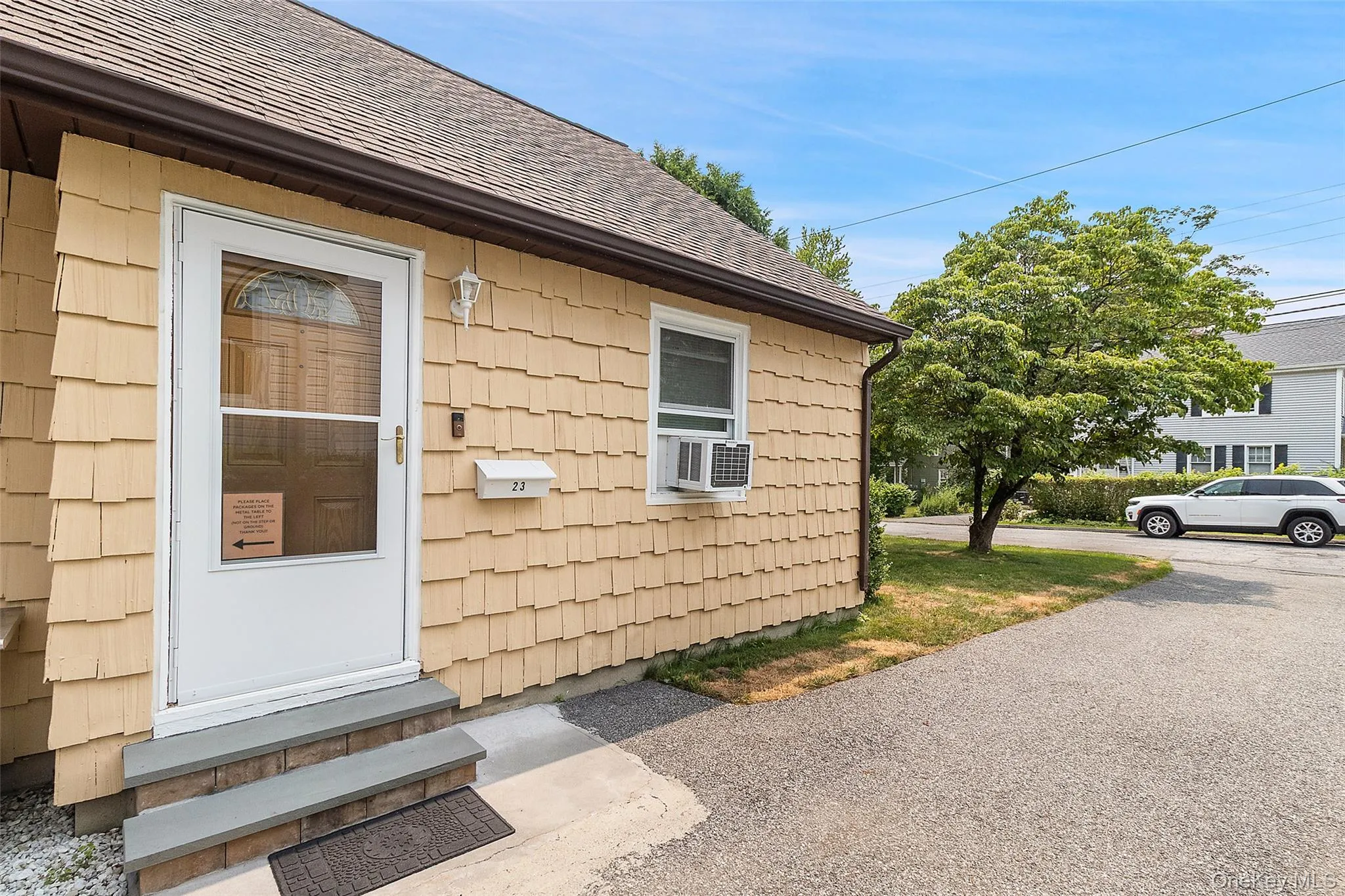 Exterior featuring cedar shake siding, a white entry door with glass paneling, and a paved driveway Exterior featuring cedar shake siding, a white entry door with glass paneling, and a paved driveway