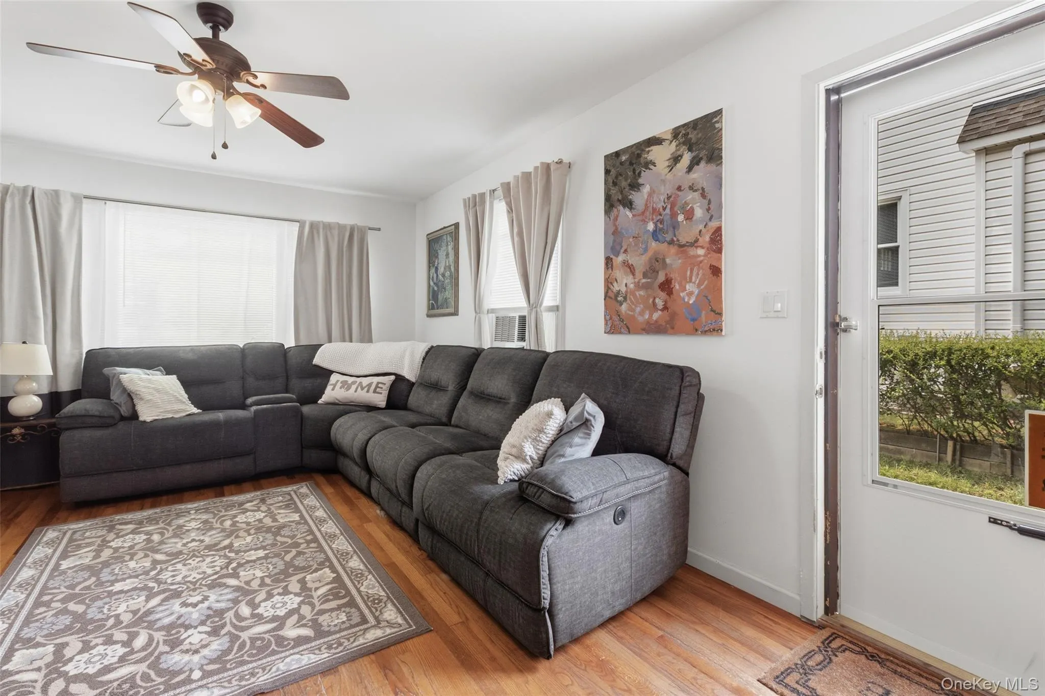 Living area featuring wood-finish flooring, white walls, and a multi-speed ceiling fan with integrated lighting Living area featuring wood-finish flooring, white walls, and a multi-speed ceiling fan with integrated lighting