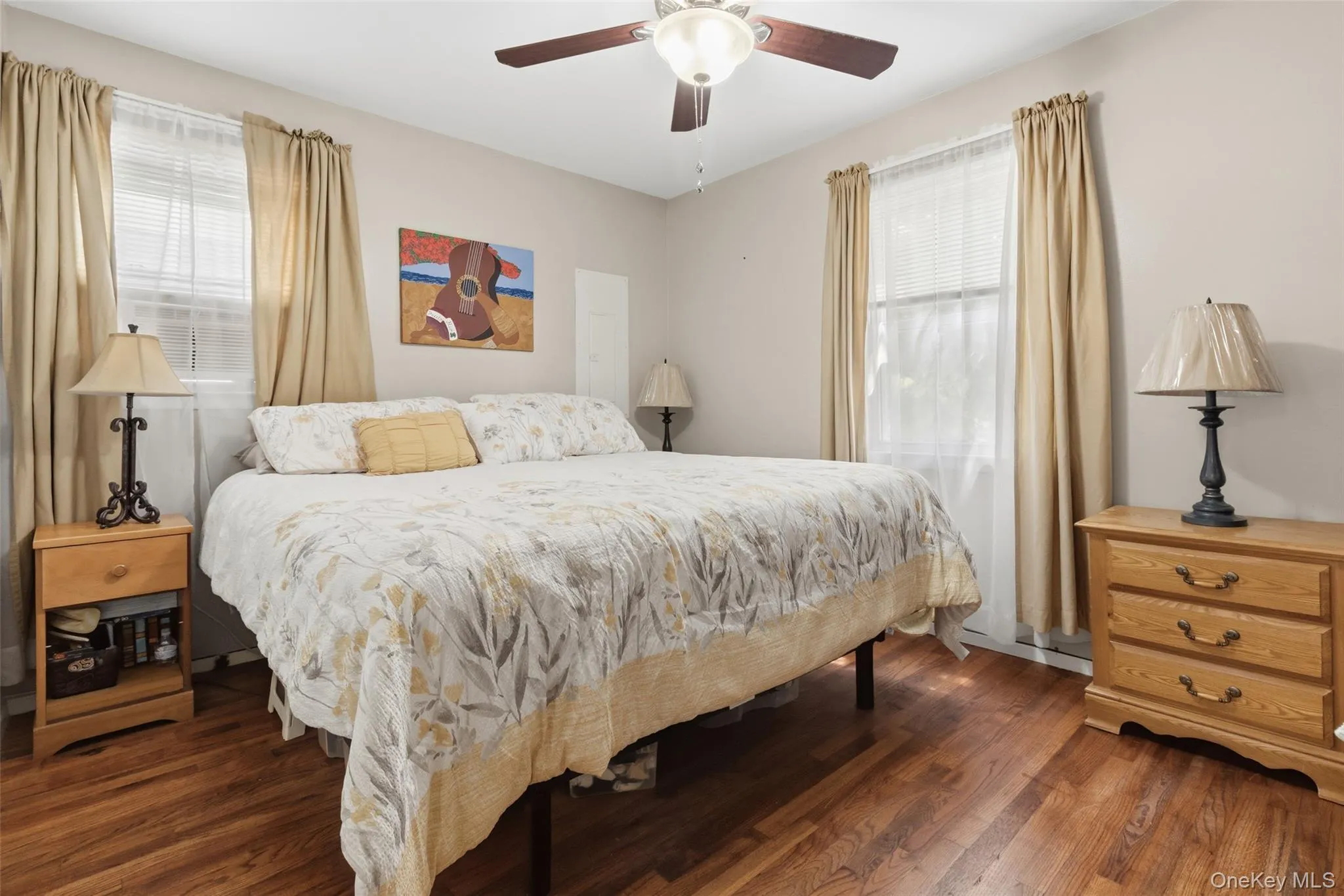 Room featuring wood-finish flooring, two windows with blinds and drapes, and a ceiling fan with integrated lighting Room featuring wood-finish flooring, two windows with blinds and drapes, and a ceiling fan with integrated lighting