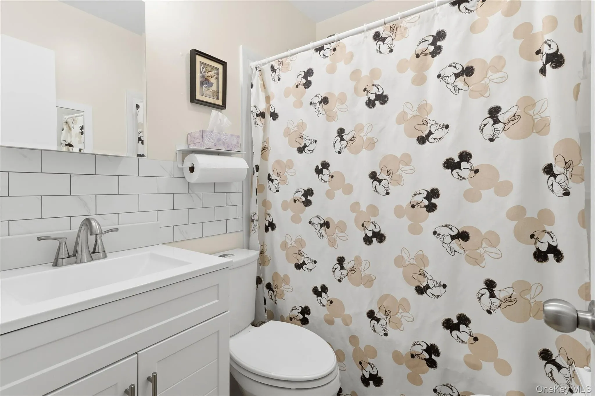 Bathroom featuring a white vanity with integrated sink, brushed nickel faucet, subway tile backsplash, and wall-mounted mirror Bathroom featuring a white vanity with integrated sink, brushed nickel faucet, subway tile backsplash, and wall-mounted mirror