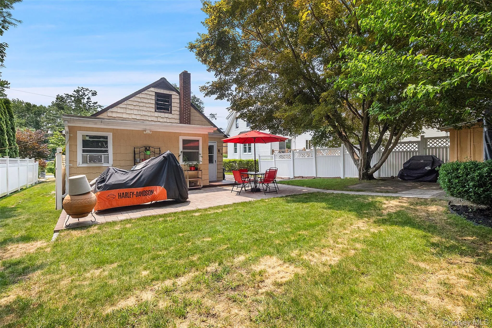 Rear exterior featuring a spacious patio, mature trees, a white picket fence, and a dormer window Rear exterior featuring a spacious patio, mature trees, a white picket fence, and a dormer window