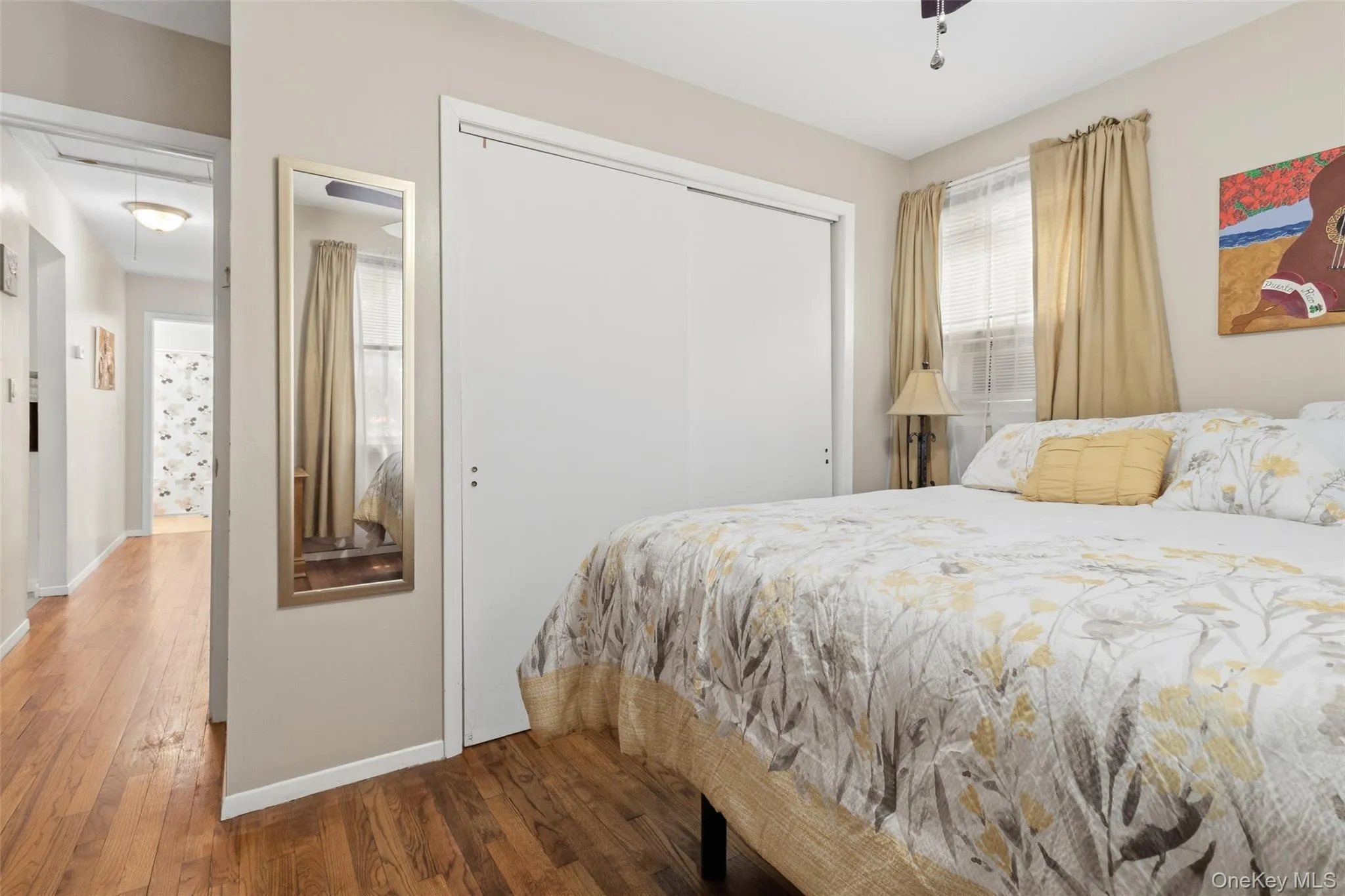 Primary bedroom featuring wood-finish flooring, a window with blinds and drapes, and a ceiling fan Primary bedroom featuring wood-finish flooring, a window with blinds and drapes, and a ceiling fan