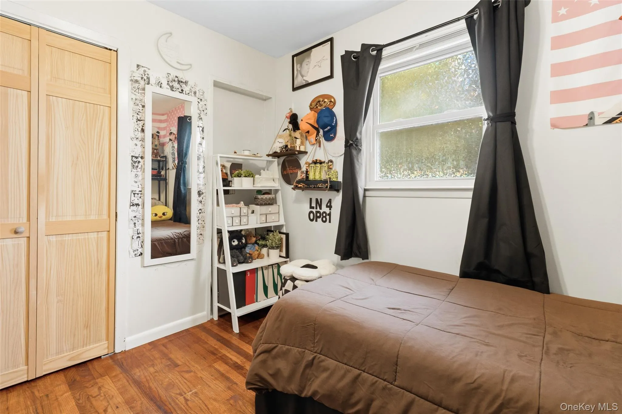 Hardwood flooring throughout featuring natural wood bi-fold closet doors, a white shelving unit, and a window with a white frame Hardwood flooring throughout featuring natural wood bi-fold closet doors, a white shelving unit, and a window with a white frame