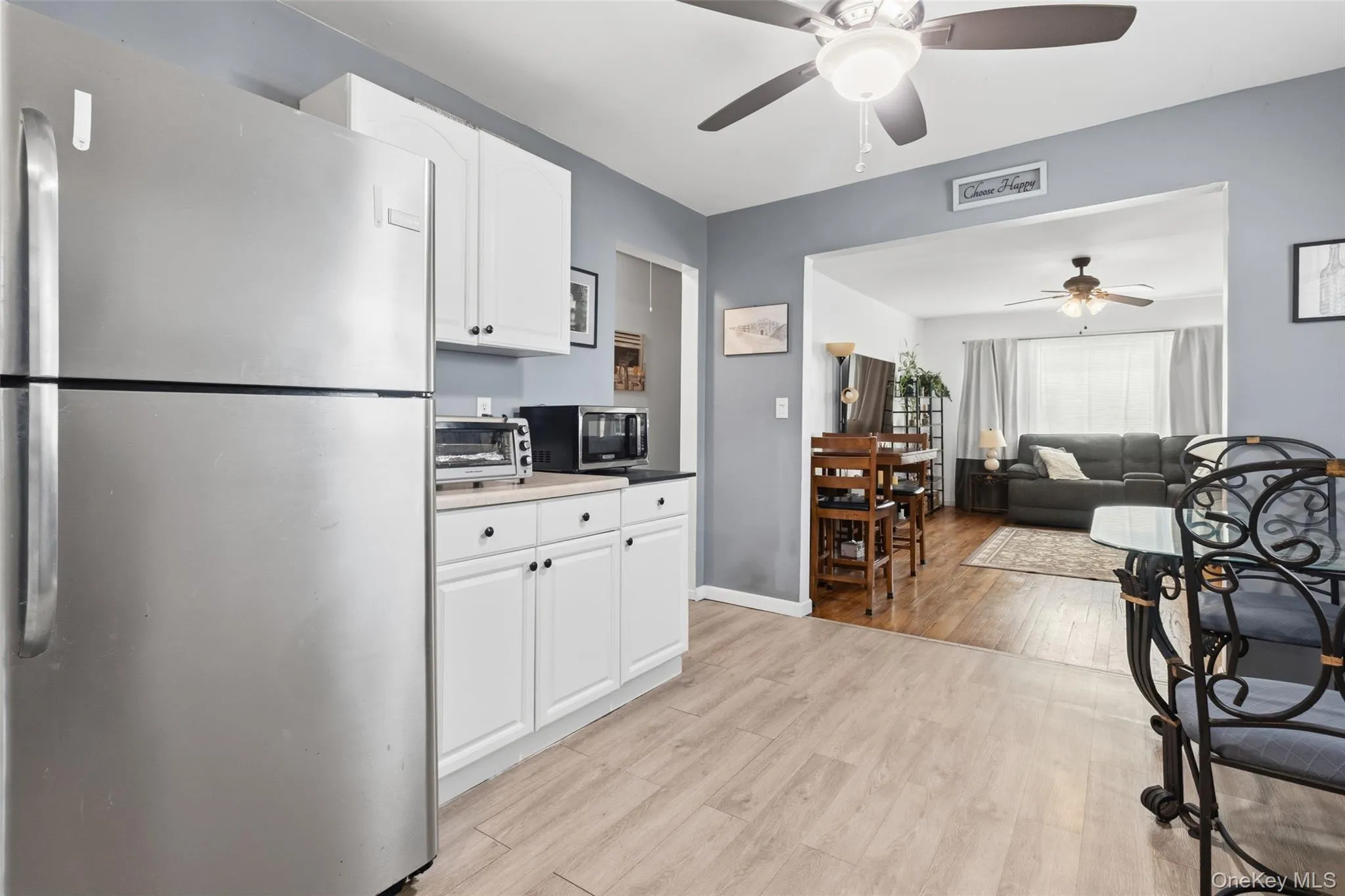 Kitchen featuring white cabinetry with dark hardware, stainless steel refrigerator, light wood-finish flooring, and a ceiling fan with integrated lighting Kitchen featuring white cabinetry with dark hardware, stainless steel refrigerator, light wood-finish flooring, and a ceiling fan with integrated lighting