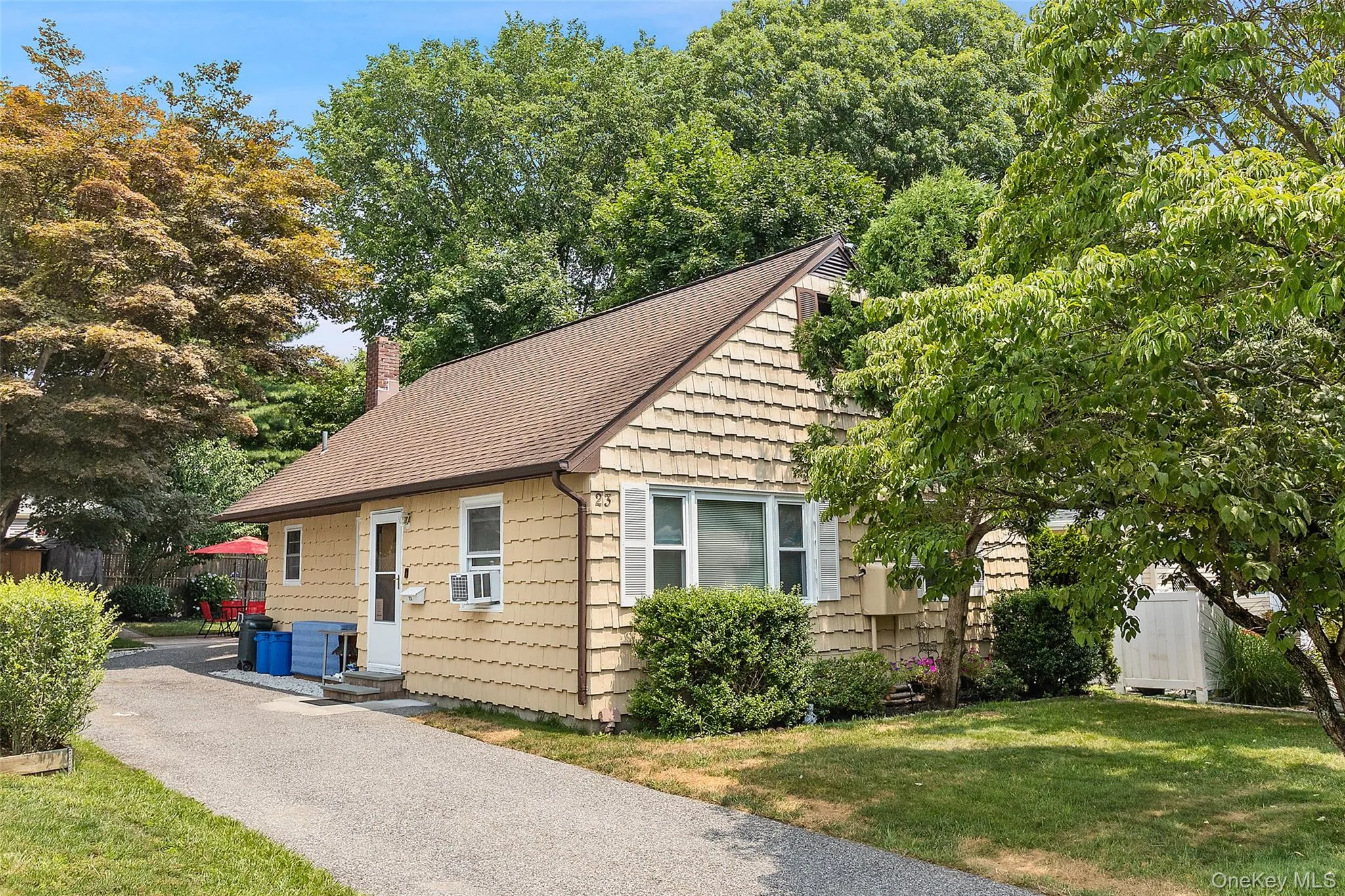 Exterior featuring horizontal siding, a shingle roof, chimney, paved driveway, and mature landscaping Exterior featuring horizontal siding, a shingle roof, chimney, paved driveway, and mature landscaping