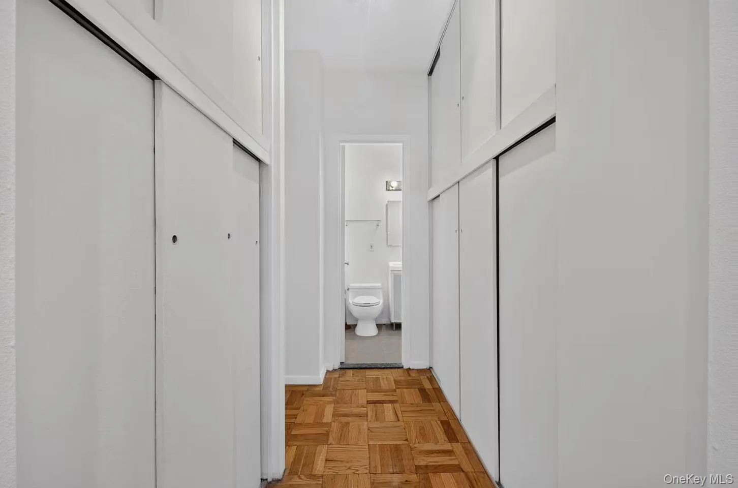 Hallway featuring wood-finish parquet flooring and white sliding closet doors Hallway featuring wood-finish parquet flooring and white sliding closet doors