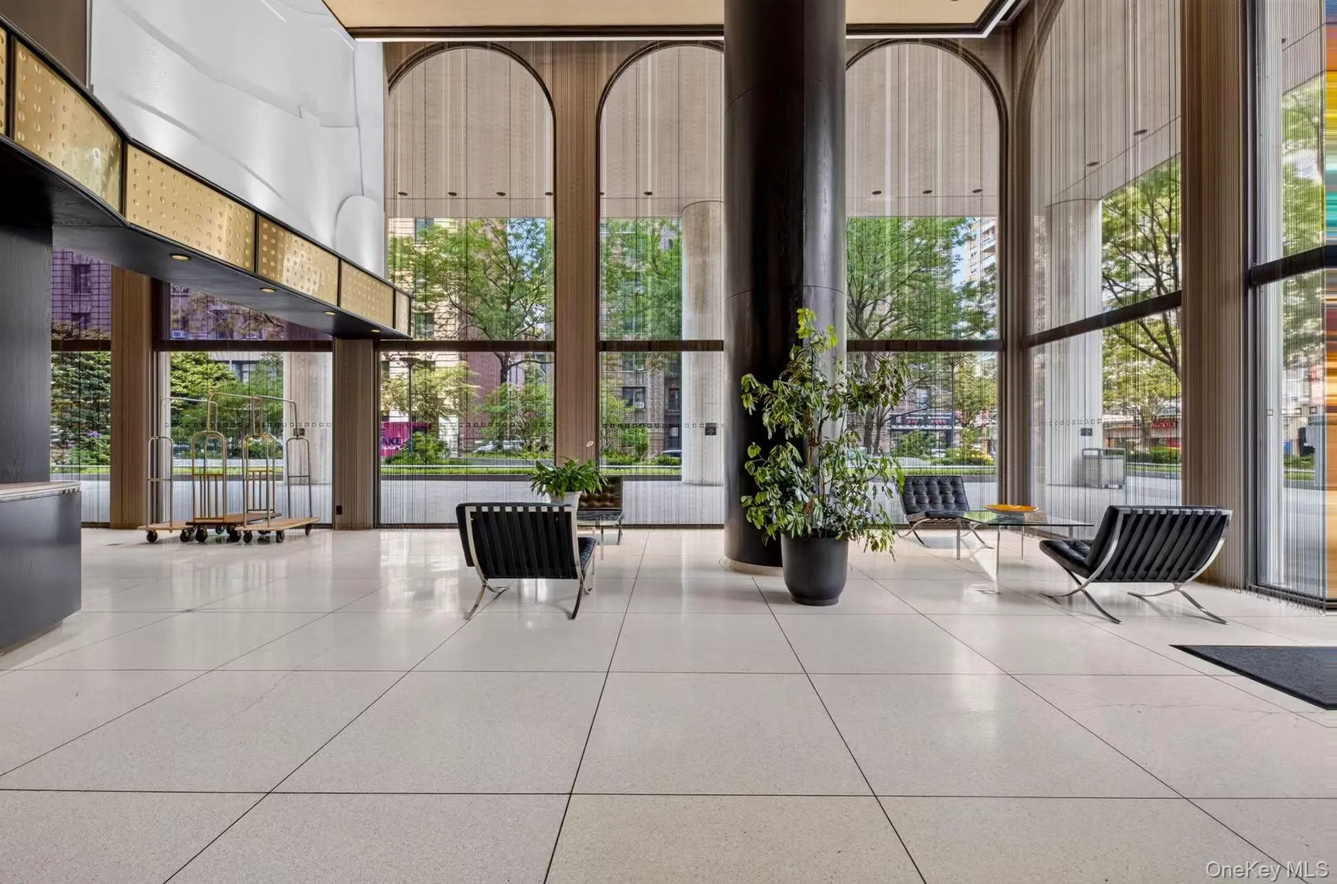 Spacious lobby featuring polished tiled flooring, floor-to-ceiling arched windows, and a prominent dark architectural column Spacious lobby featuring polished tiled flooring, floor-to-ceiling arched windows, and a prominent dark architectural column
