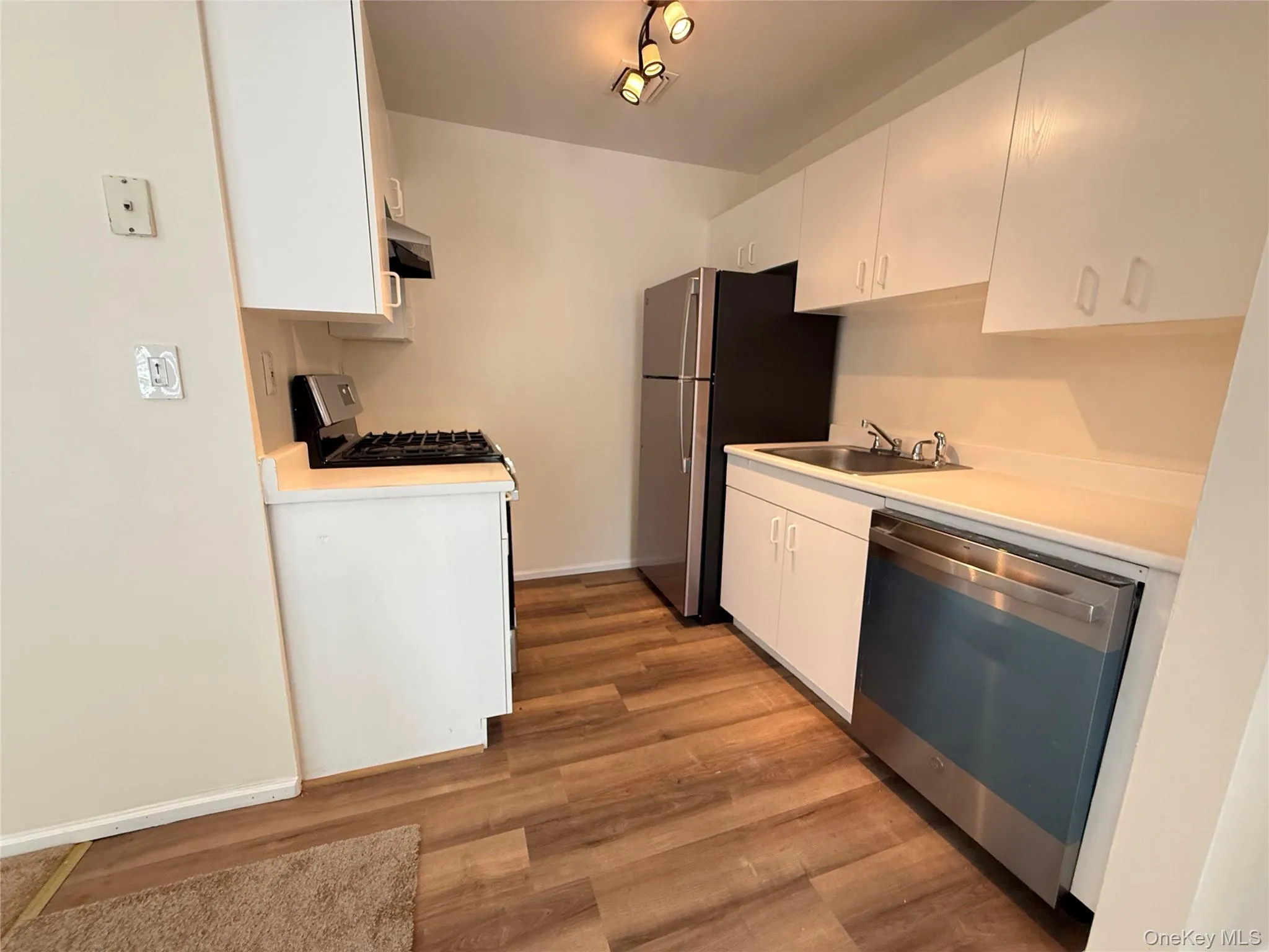 Kitchen featuring wood-finish flooring, white cabinetry, and stainless steel appliances Kitchen featuring wood-finish flooring, white cabinetry, and stainless steel appliances